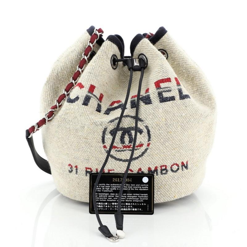 This Chanel Deauville Drawstring Bucket Bag Canvas Medium, crafted in neutral printed canvas, features woven-in canvas chain strap, CC logo with Chanel's famous Parisian store address on front, and silver-tone hardware. Its drawstring closure opens