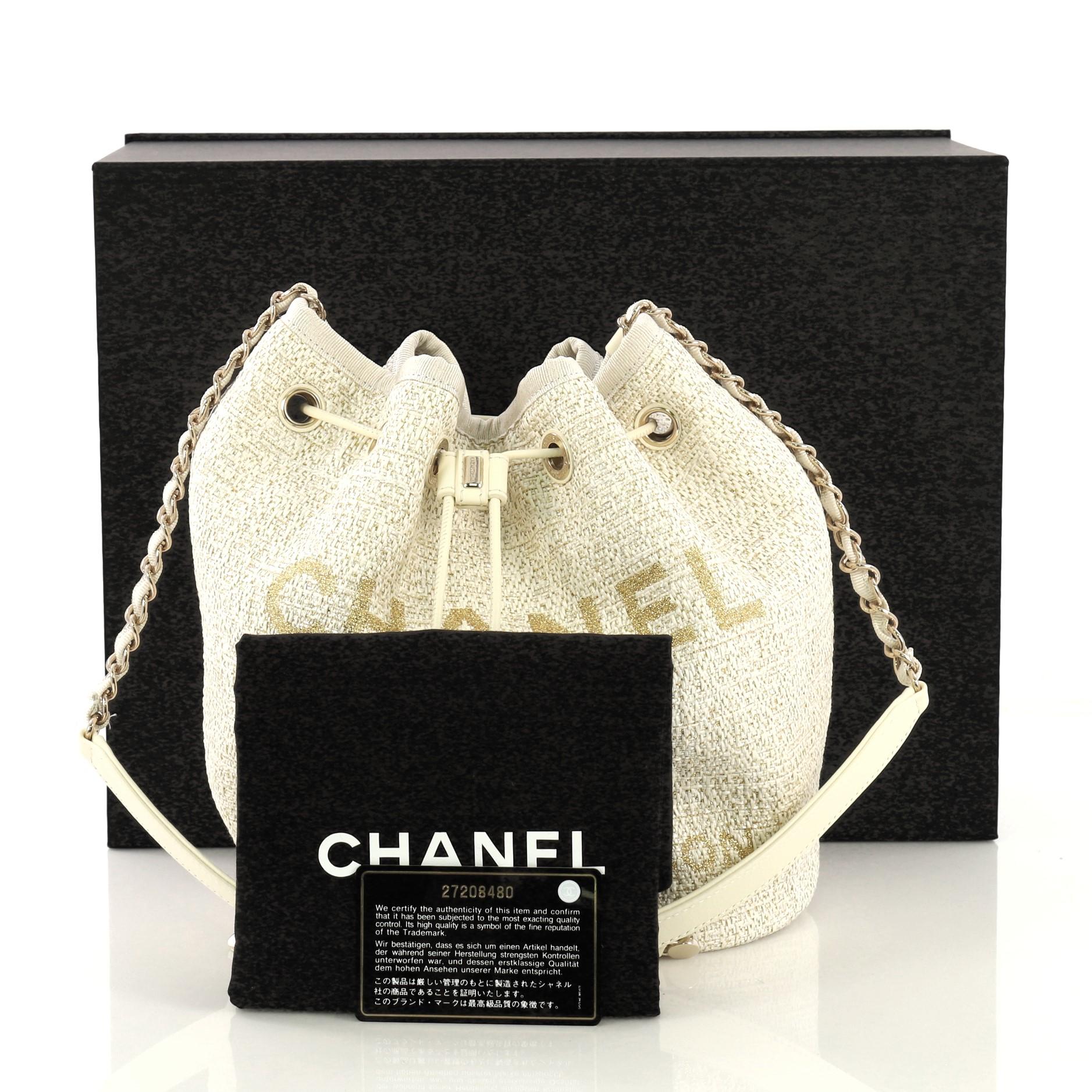 This Chanel Deauville Drawstring Bucket Bag Raffia Medium, crafted in white and gold raffia, features woven-in canvas chain strap, CC logo with Chanel's famous Parisian store address on front, and gold-tone hardware. Its drawstring closure opens to