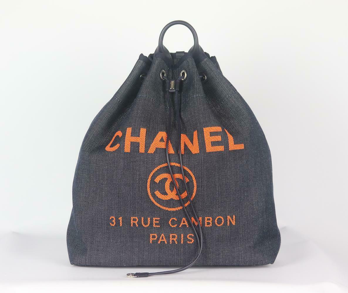 Made in Italy, this beautiful Chanel Deauville backpack has been made from navy canvas and navy leather exterior with black fabric interior, this piece is decorated with Chanel's logo in orange on the front and finished with chain and leather straps