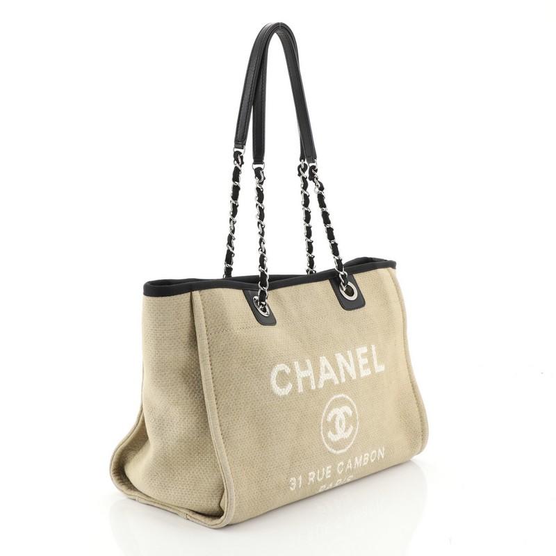 This Chanel Deauville Tote Canvas Small, crafted in neutral canvas, features dual woven-in canvas chain straps with shoulder pads, CC logo with Chanel's famous Parisian store address on front, and silver-tone hardware. Its magnetic snap closure