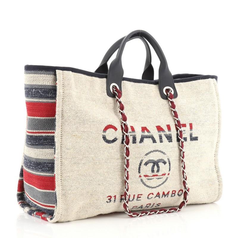 This Chanel Deauville Tote Canvas with Striped Detail Large, crafted in neutral canvas with multicolor striped detail, features dual rolled top handles, dual woven-in canvas chain straps, and silver-tone hardware. Its magnetic snap closure opens to