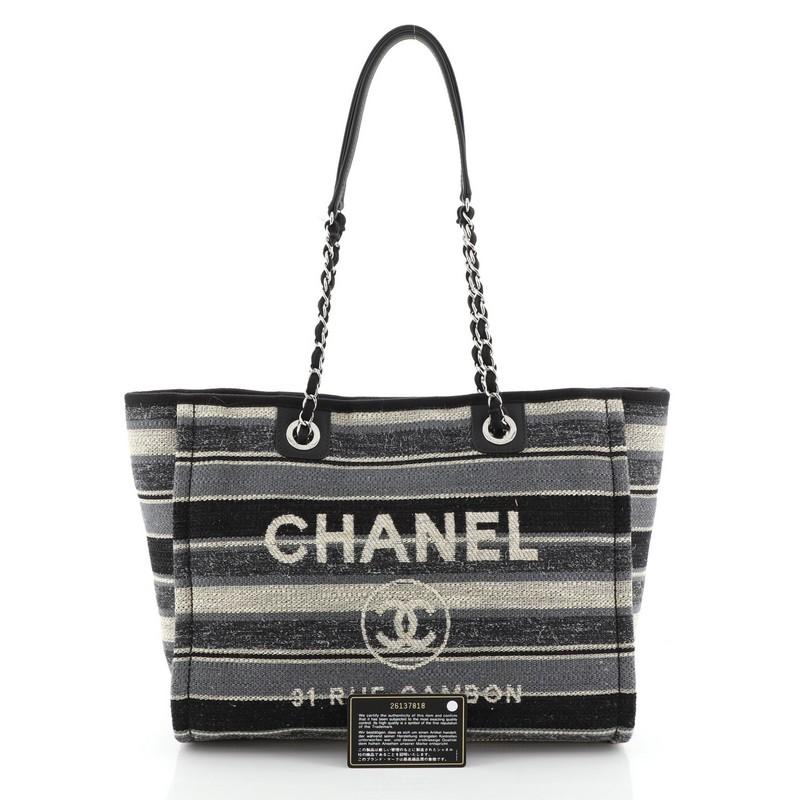 This Chanel Deauville Tote Canvas with Striped Detail Small, crafted in blue canvas with multicolor striped detail, features dual woven-in canvas chain straps, printed CC logo, and silver-tone hardware. Its magnetic snap closure opens to a neutral