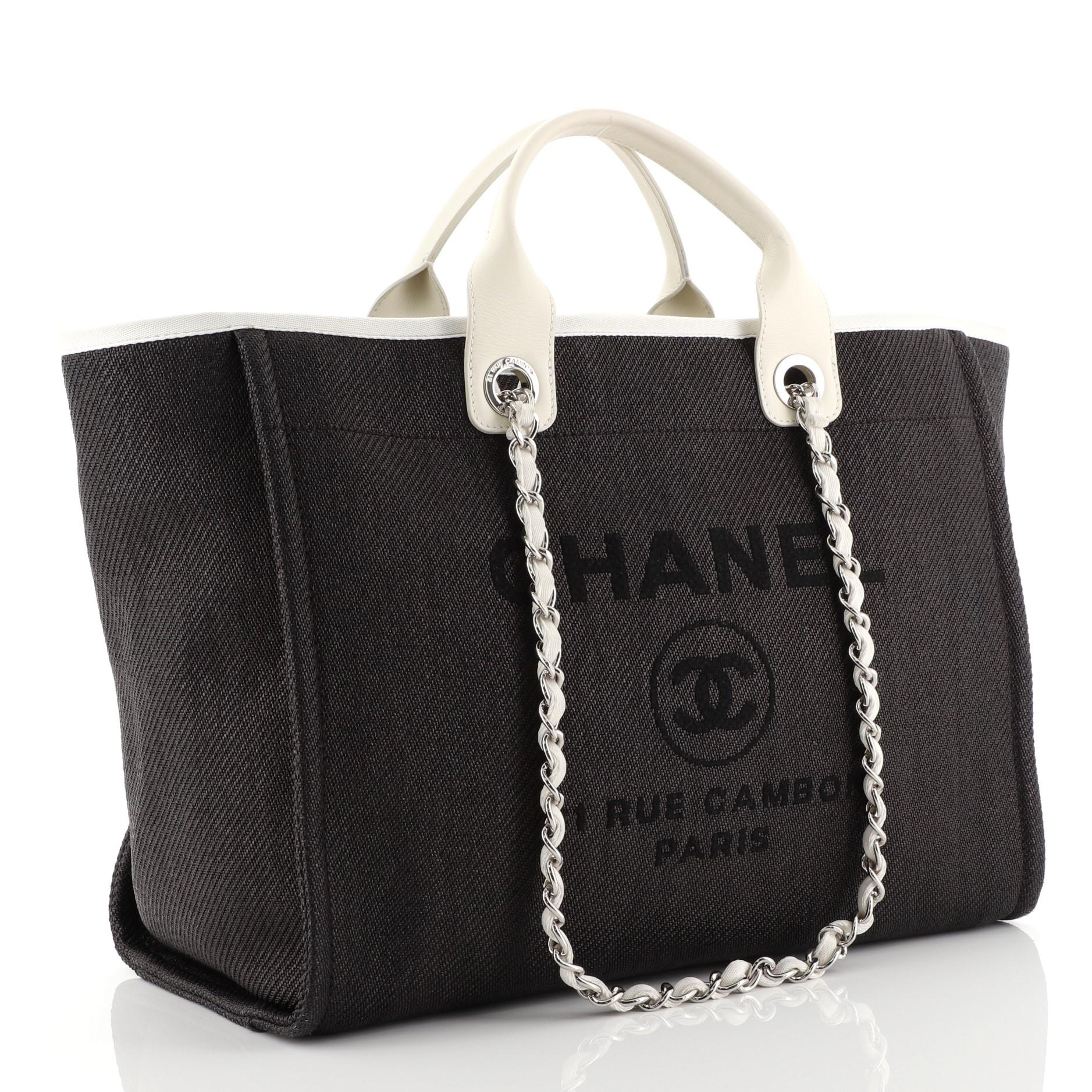 This Chanel Deauville Tote Raffia Large, crafted from black raffia, features dual leather handles, woven-in canvas chain straps, and silver-tone hardware. Its magnetic snap closure opens to a black fabric interior with slip and zip pockets. Hologram