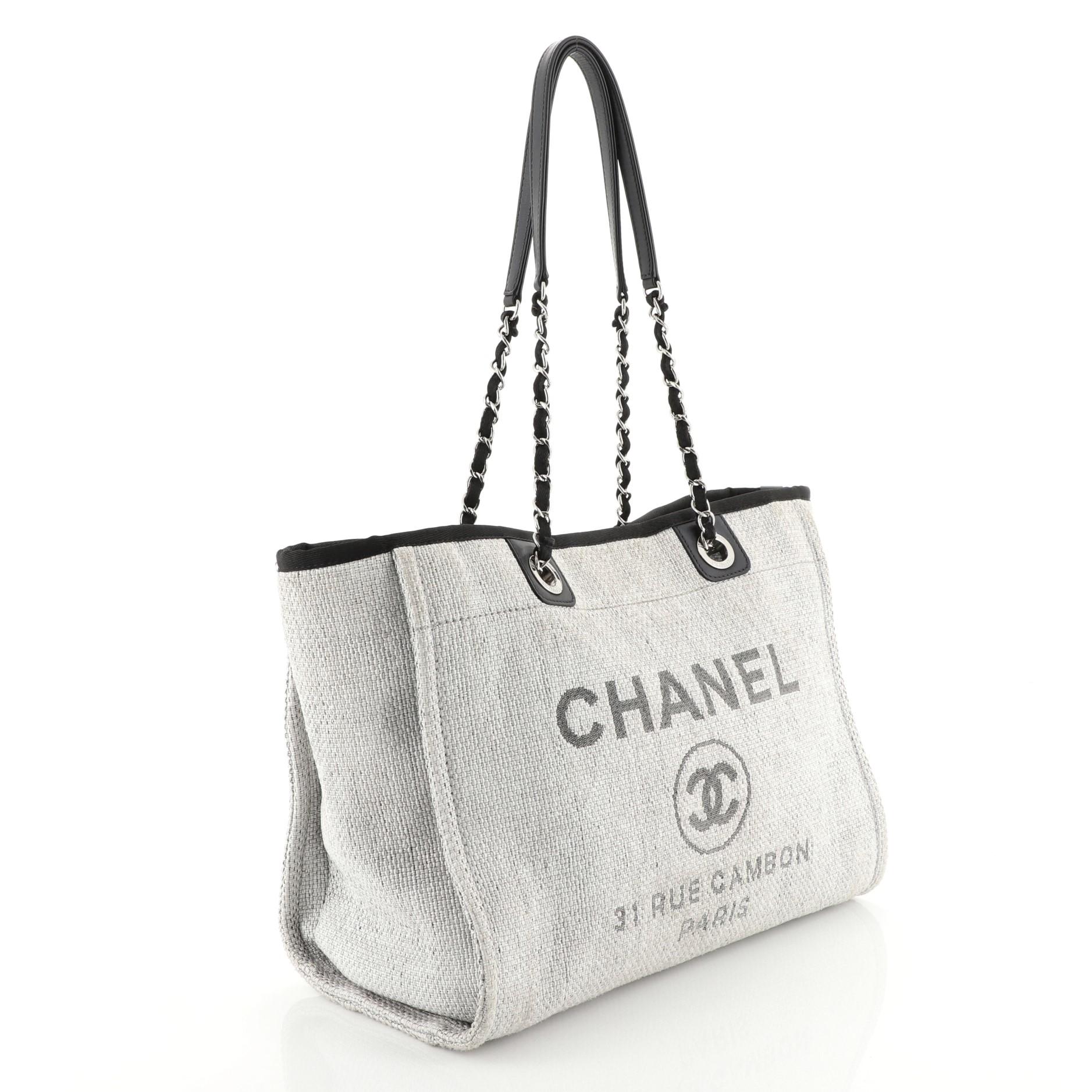 This Chanel Deauville Tote Raffia Small, crafted in gray raffia, features dual woven-in canvas chain straps and silver-tone hardware. Its magnetic snap closure opens to a black fabric interior with slip and zip pockets. Hologram sticker reads: