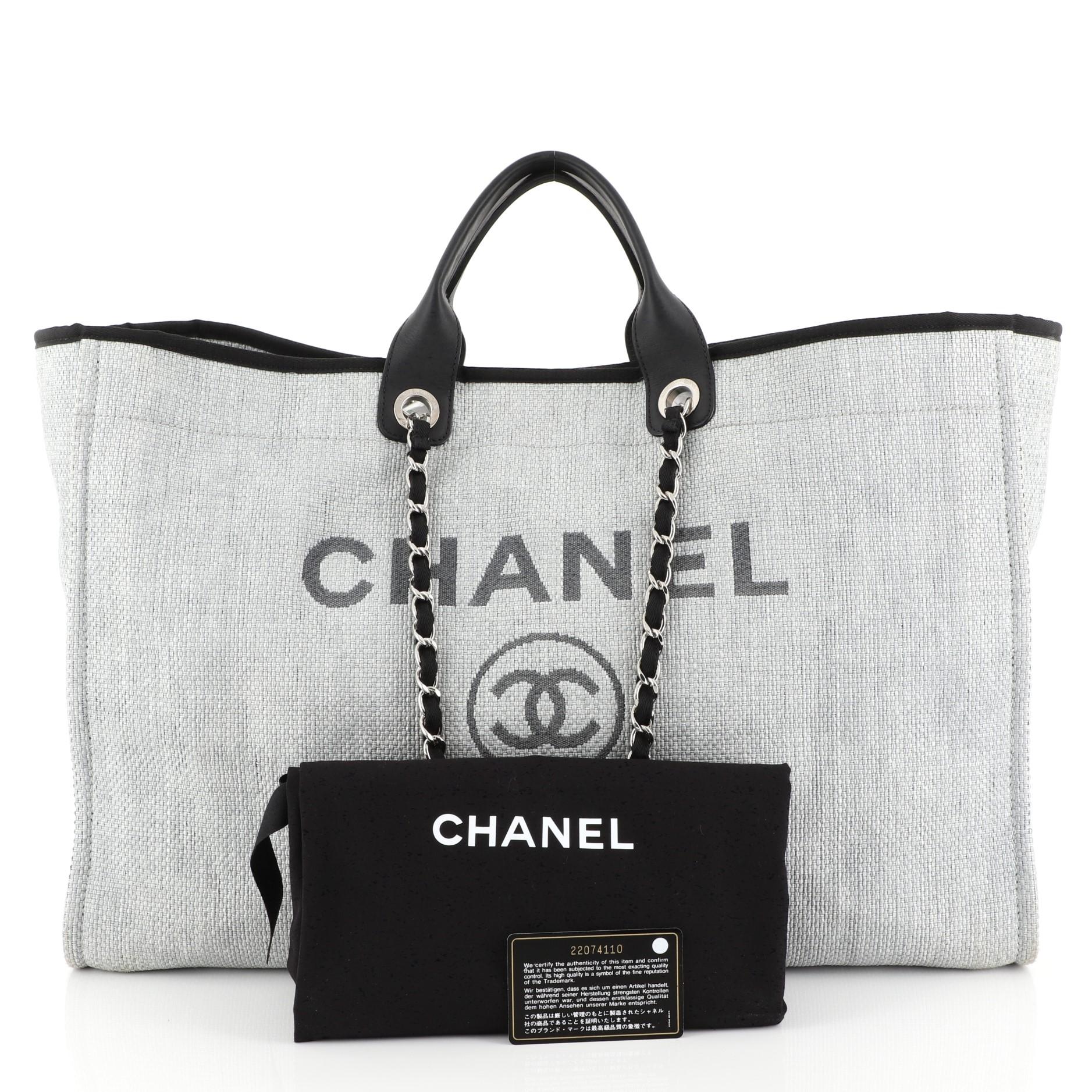 This Chanel Deauville Tote Raffia XL, crafted from gray raffia, features dual leather handles, woven-in canvas chain straps, and silver-tone hardware. Its magnetic snap closure opens to a black fabric interior with slip and zip pockets. Hologram