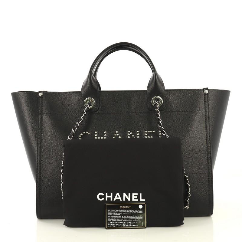 This Chanel Deauville Tote Studded Caviar Medium, crafted in black studded caviar leather, features dual woven-in leather chain straps, dual top handles, studded logo at the front, and silver-tone hardware. Its magnetic snap closure opens to a black