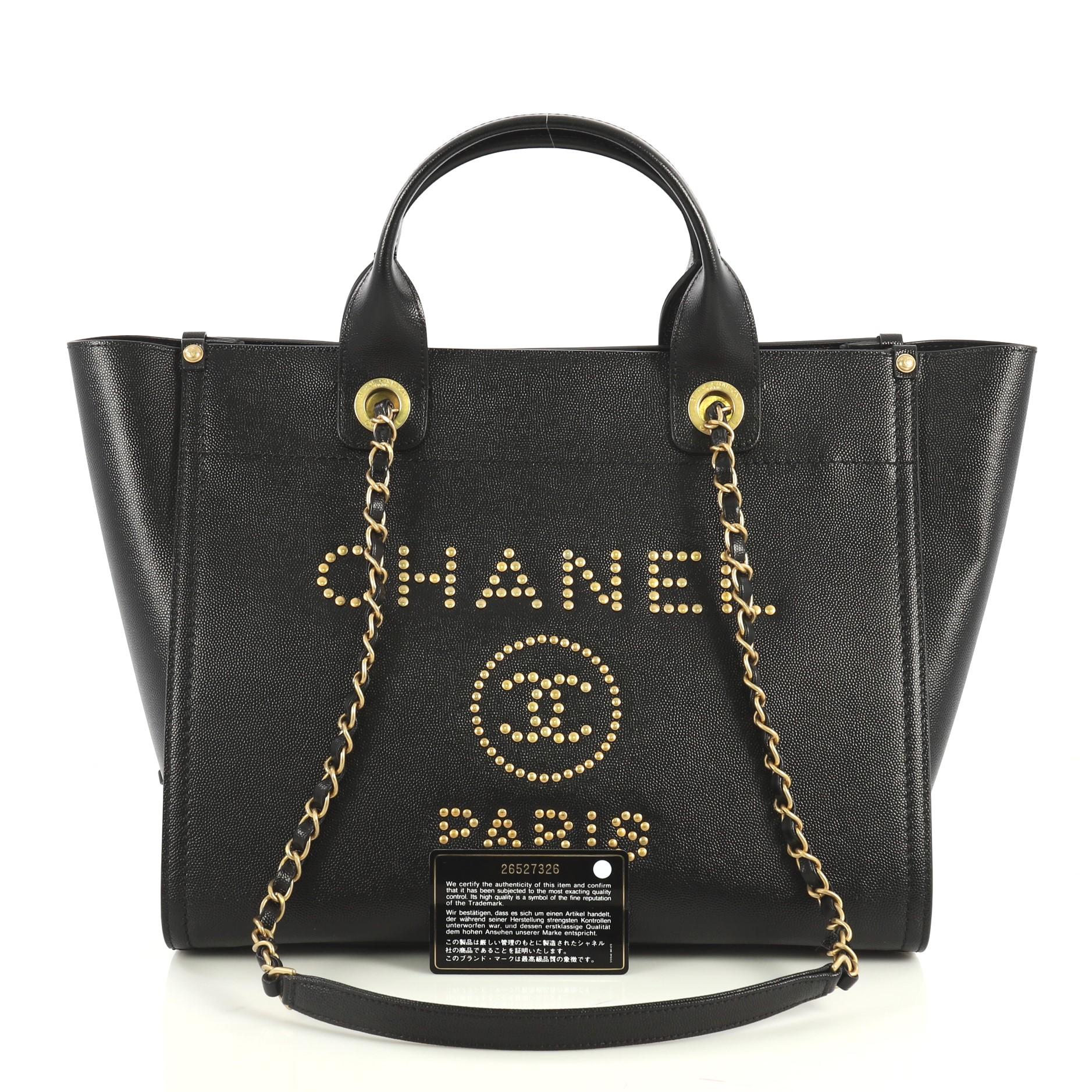 This Chanel Deauville Tote Studded Caviar Small, crafted in black studded caviar leather, features dual woven-in leather chain straps, dual top handles, studded logo at the front, and aged gold-tone hardware. Its magnetic snap closure opens to a