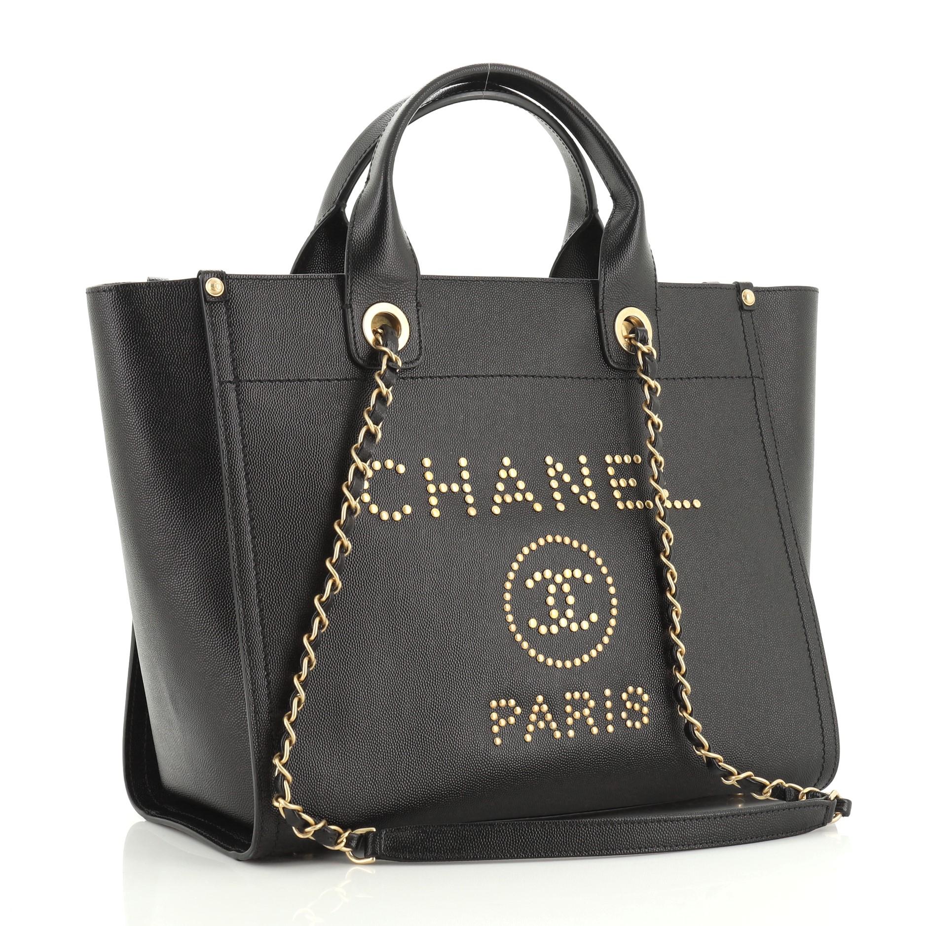 This Chanel Deauville Tote Studded Caviar Small, crafted in black studded caviar leather, features dual woven-in leather chain straps, dual top handles, studded logo at the front, and gold-tone hardware. Its magnetic snap closure opens to a black
