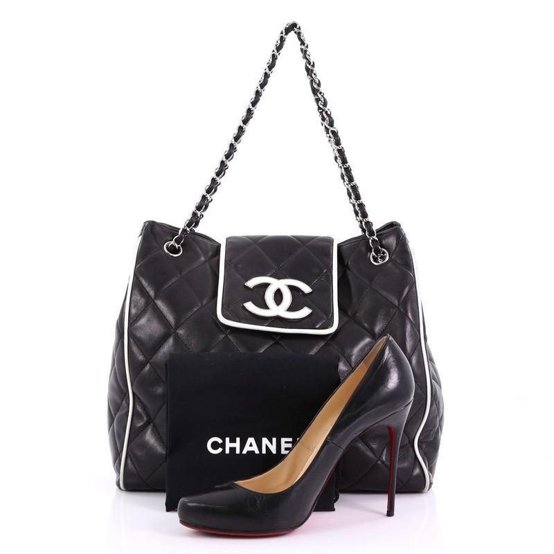 This Chanel Divine Tote Quilted Lambskin Medium, crafted in black quilted lambskin leather, features woven-in leather chain straps, white leather trim, and silver-tone hardware. It opens to a grey satin interior with zip and slip pockets. Hologram