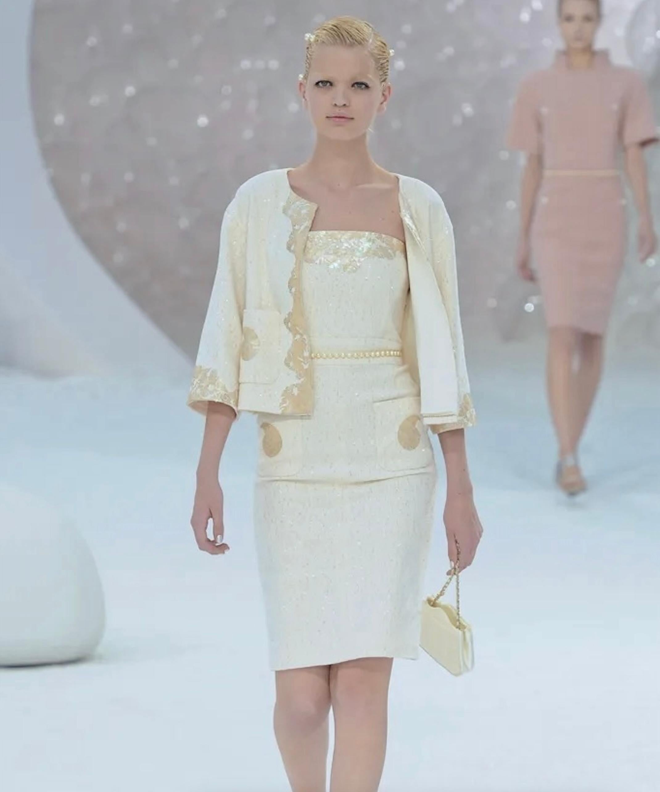 Presentado como look 5 en la pasarela Chanel Primavera 2012 del Grand Palais de París por Karl Lagerfeld, este documentado vestido de tweed marfil está destinado a la perfección nupcial. Con adornos de nácar y lentejuelas brillantes por todas