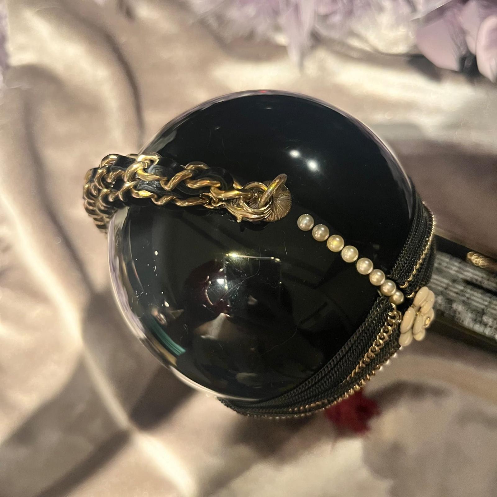 This rare, limited edition Chanel bag features a stylized doll design with a brushed gold-tone metallic face and black enamel body. Adorned with intricate details including a pearl and chain-embellished turban, a crystal bindi, and a signature
