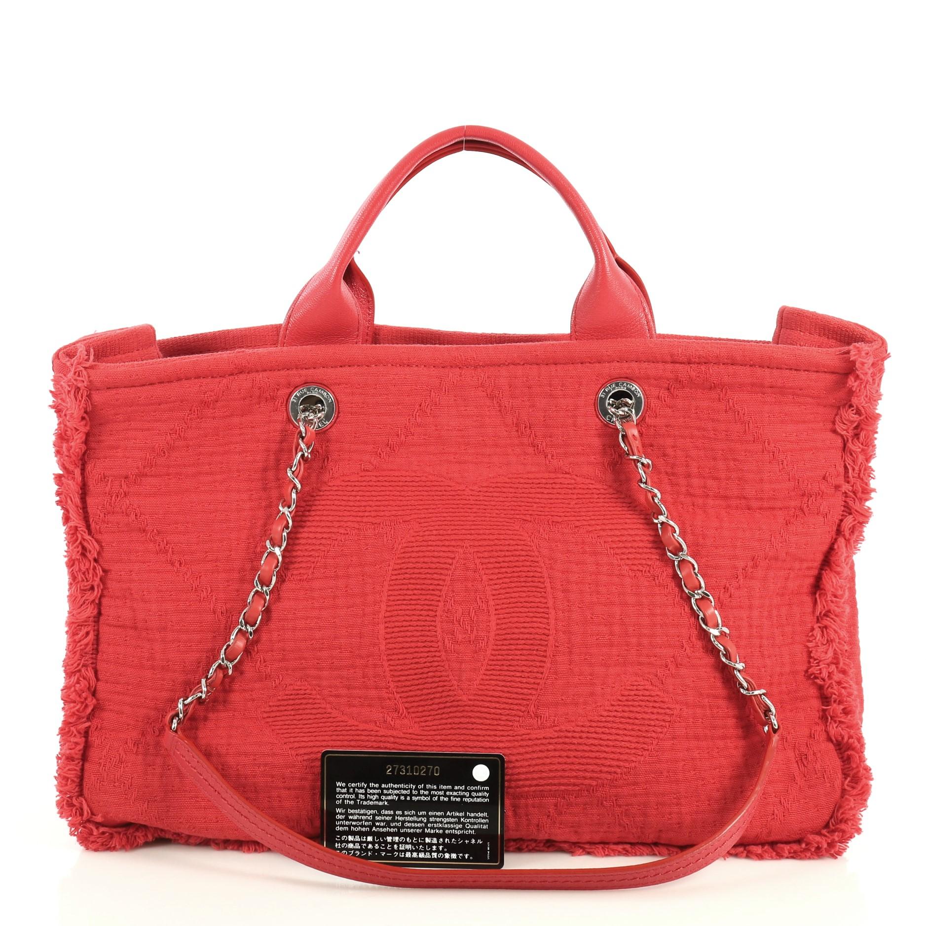 This Chanel Double Face Deauville Tote Fringe Quilted Canvas Medium, crafted in red quilted canvas, features dual woven-in leather chain straps, dual top handles, CC logo at the front, and silver-tone hardware. Its magnetic snap closure opens to a
