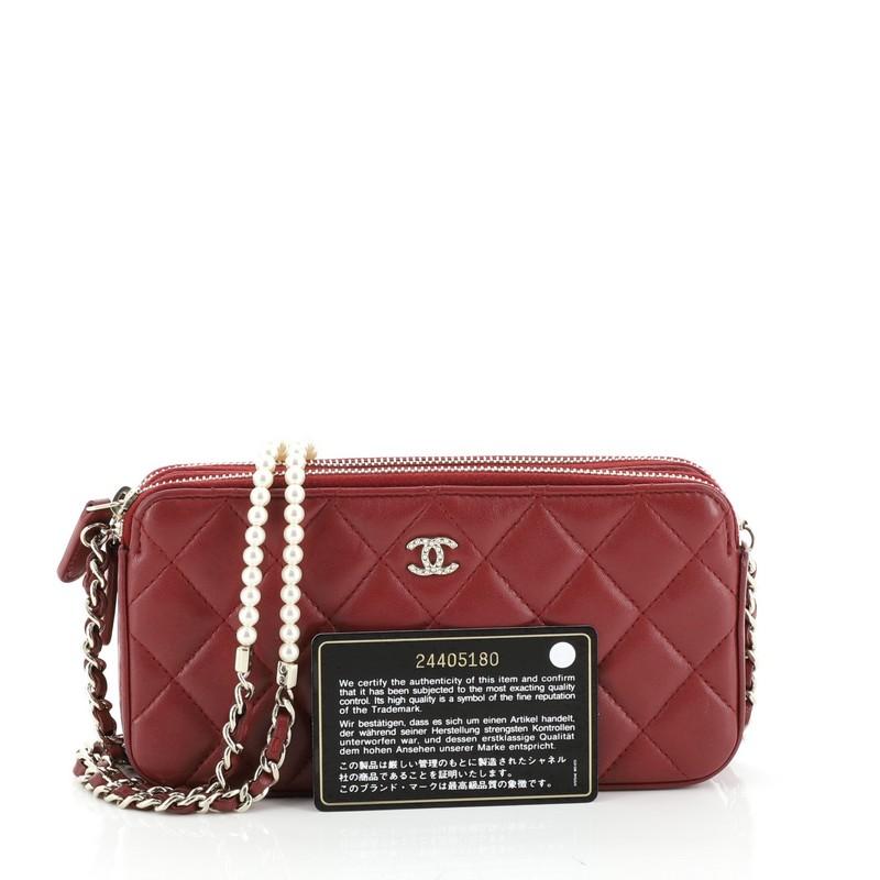 This Chanel Double Zip Clutch with Pearl Chain Quilted Lambskin, crafted from red quilted lambskin, features woven-in leather chain straps with pearls, embellished CC logo, and gold-tone hardware. Its dual zip and open center compartment opens to a