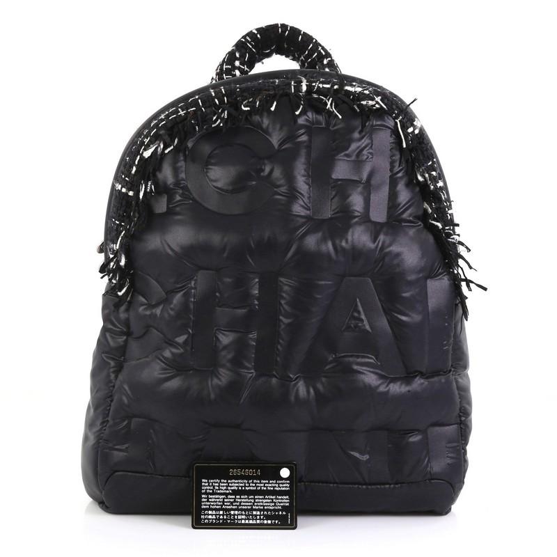 This Chanel Doudoune Backpack Embossed Nylon with Tweed Medium, crafted from black embossed nylon with tweed, features a top handle, adjustable shoulder straps, large embossed CHANEL letters, and silver-tone hardware. Its zip closure opens to a