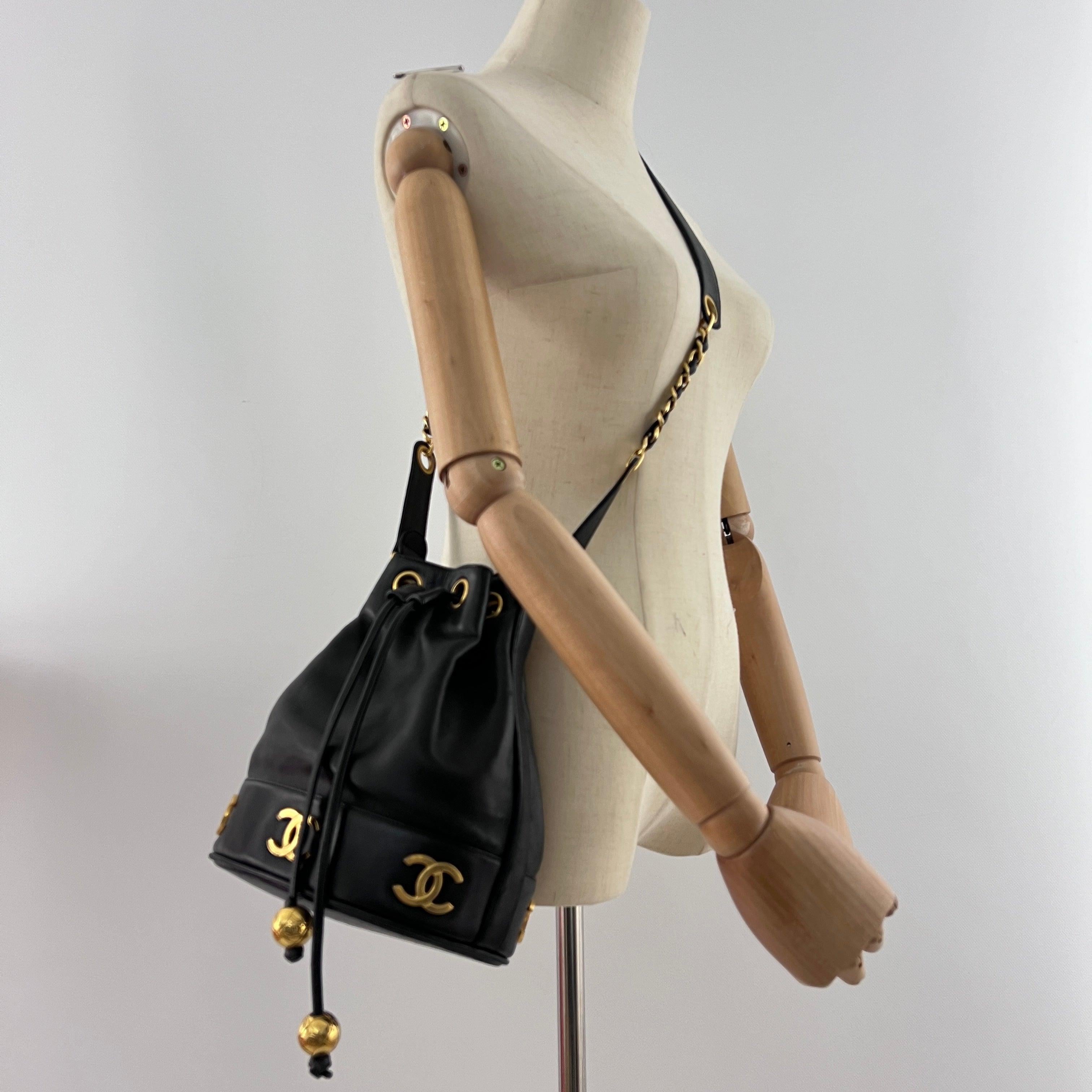 Magnifique sac à main CHANEL modèle Seau, réalisé en cuir d’agneau noir et rehaussé d’une bijouterie dorée. Pièce iconique des années 1990, ce modèle illustre à merveille l’esprit de liberté et de modernité insufflé par Karl Lagerfeld à la