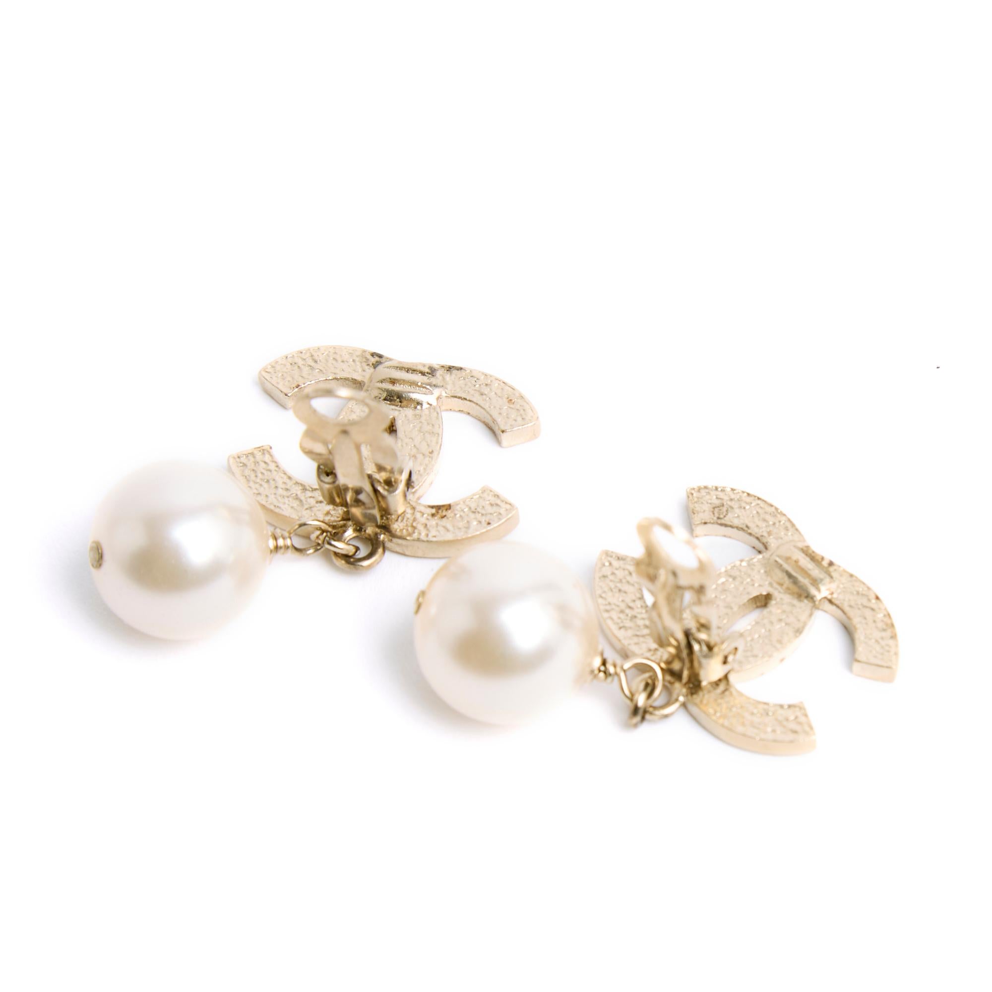 Chanel Clip-Ohrringe, bestehend aus einem großen Chanel CC-Logo aus fein gestepptem, goldenem Metall und einem runden, ausgefallenen Perlen-Anhänger. Breite 2 cm x Höhe 3,45 cm. Die Ohrringe sind in sehr gutem Zustand, klassisch schick und leuchtend