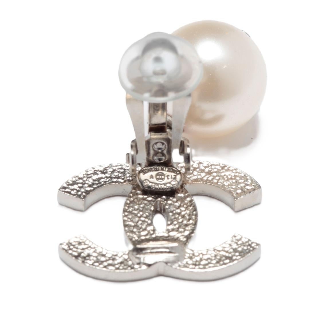 Chanel Clip-Ohrringe, bestehend aus einem großen Chanel CC-Logo aus fein gestepptem, silberfarbenem Metall und einem runden, ausgefallenen Perlen-Anhänger. Breite 2 cm x Höhe 3,45 cm. Die Ohrringe werden ohne Originalrechnung oder -verpackung