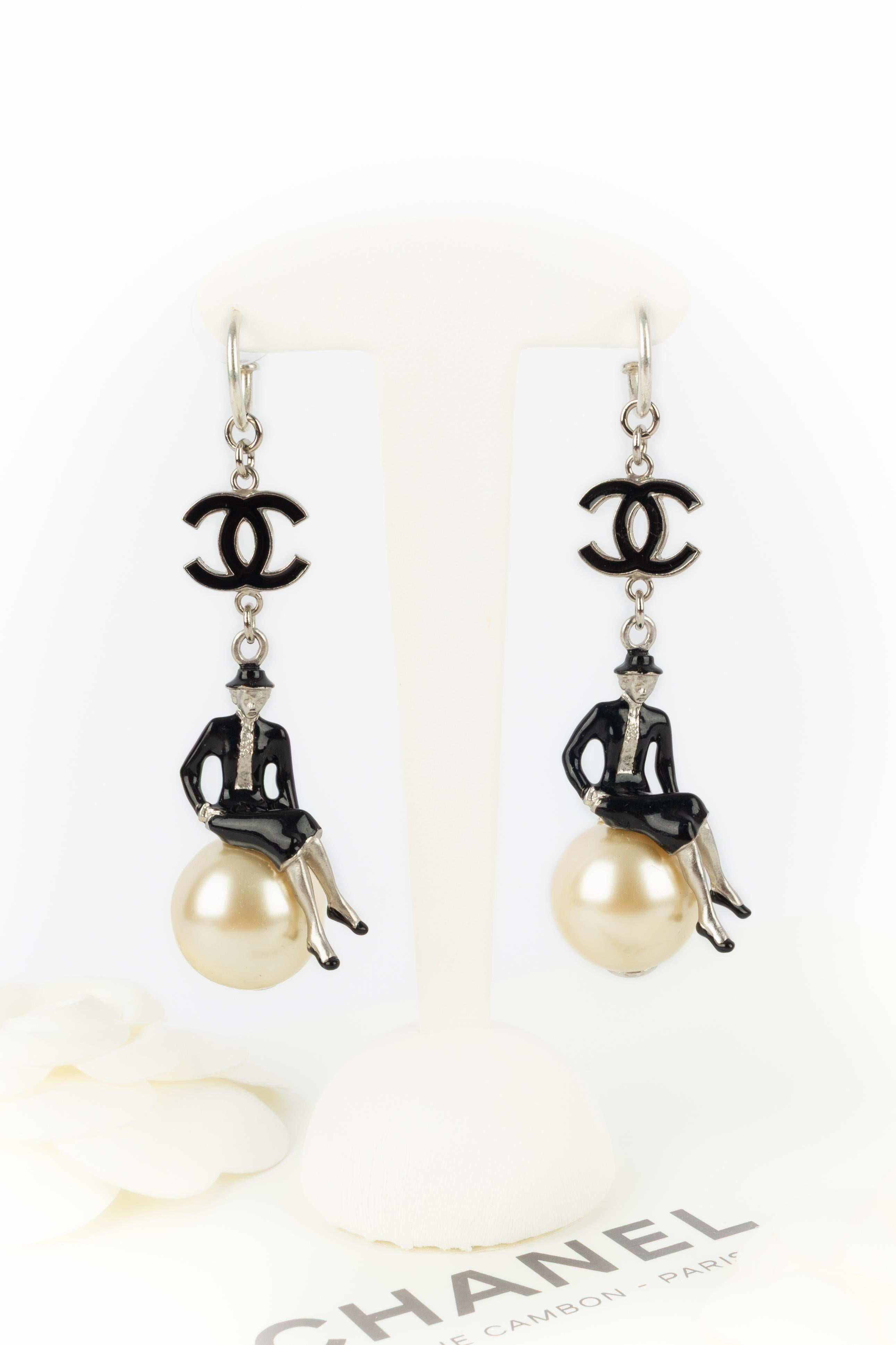 CHANEL - (Made in France) Silvery metal earrings enameled with black and representing Coco Chanel sat on a costume pearl. 2004 Spring-Summer Collection under the artistic direction of Karl Lagerfeld.

Condition:
Very good