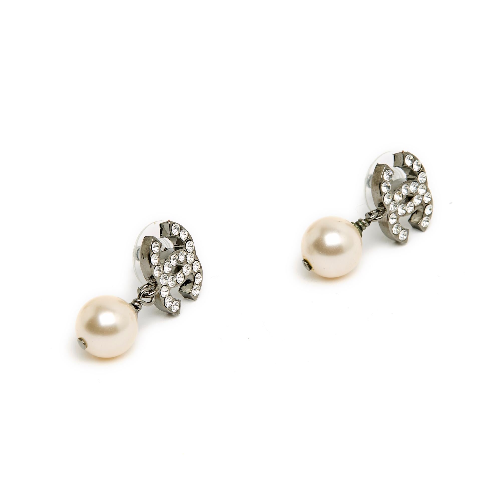 Chanel Ohrstecker, bestehend aus einem Chanel CC-Logo aus geschwärztem, silbernem Metall, das mit Strasssteinen besetzt ist, und einem runden, ausgefallenen Perlenanhänger. Breite 1,5 cm x Höhe 2,65 cm. Die Ohrringe werden ohne Rechnung oder