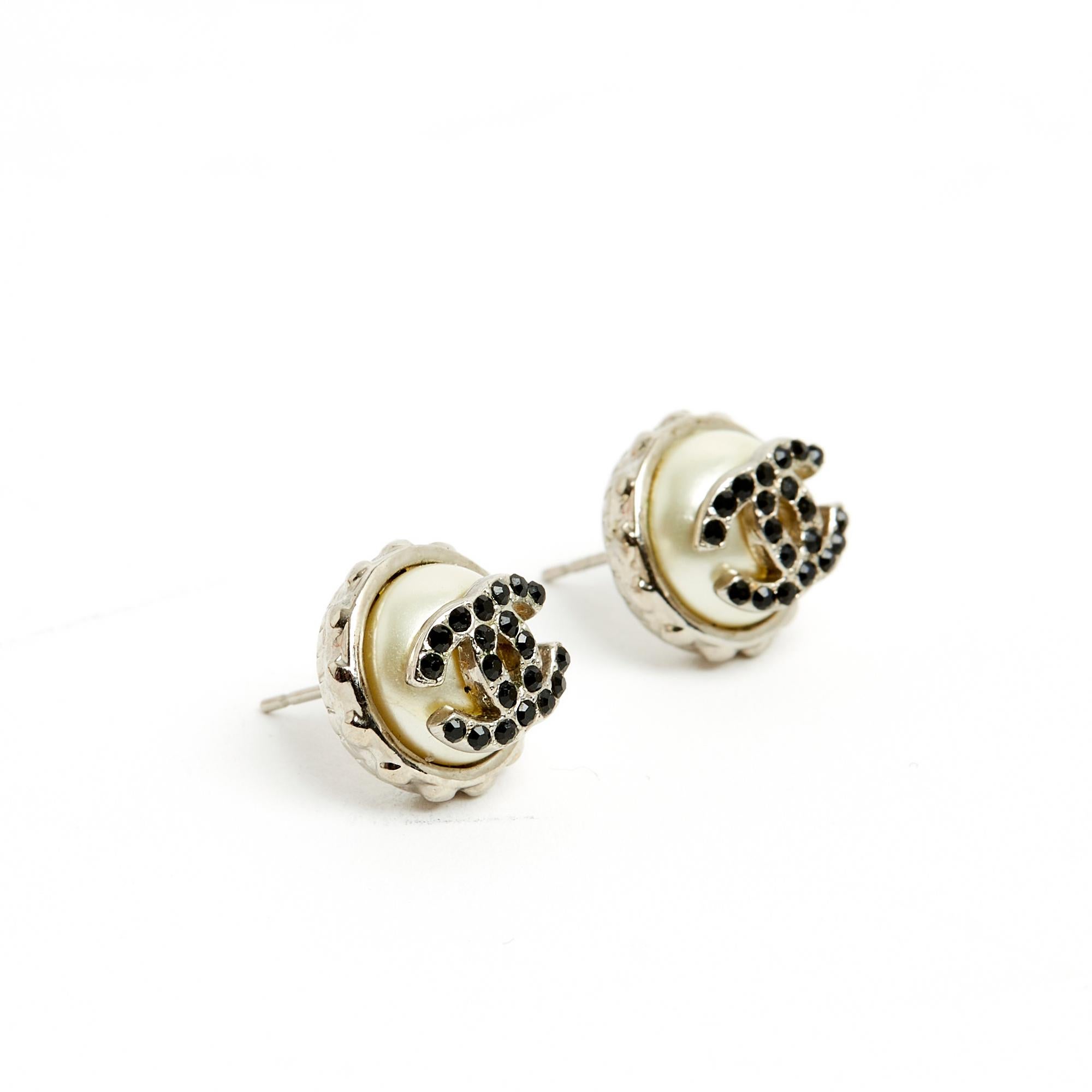 Chanel small stud earrings in silver metal composed of a half pearl topped with a small CC logo inlaid with black rhinestones. Diameter 1.35 cm. The earrings are delivered without original packaging and invoice, they are in very good condition, chic