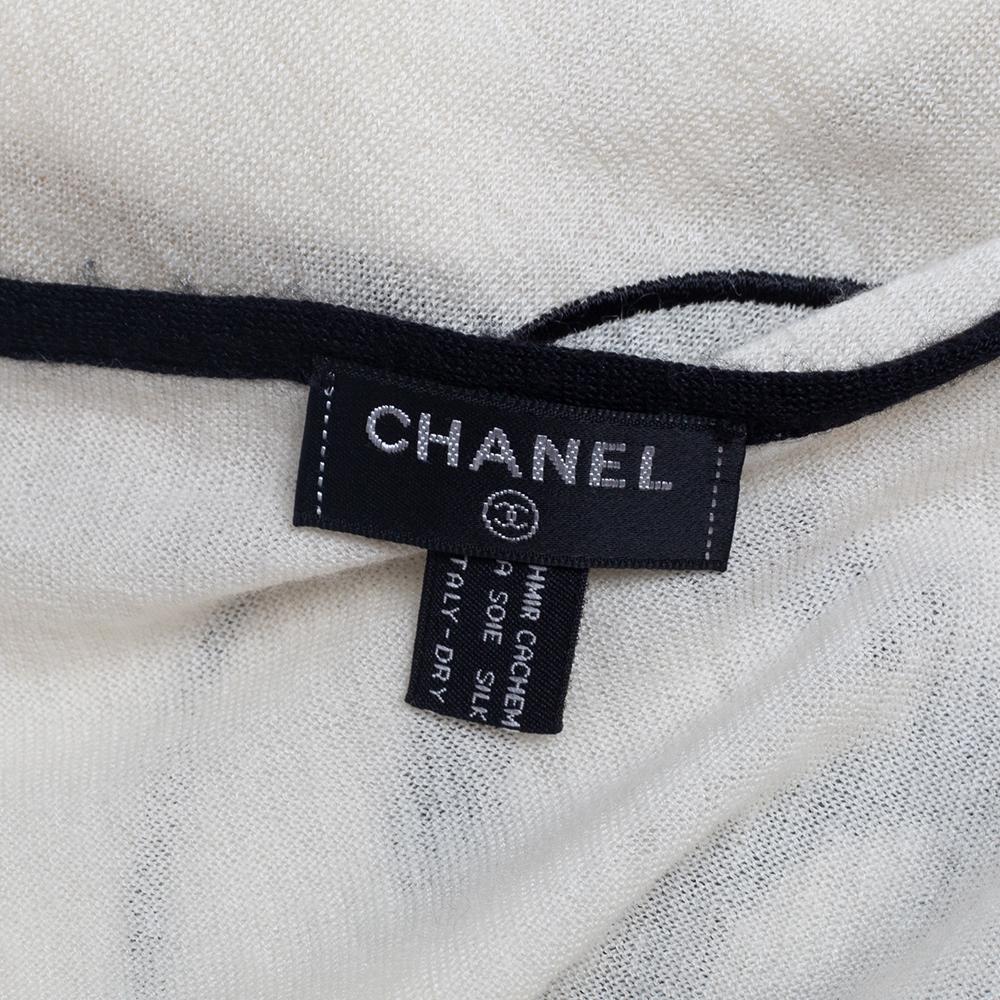 Incorporate a luxe and chic touch to your outfits by wearing this scarf from the House of Chanel. It is designed using white ecru cashmere and silk knit fabric, which is augmented with a contrasting CC-logo embroidery. It has a length of 198 cm.