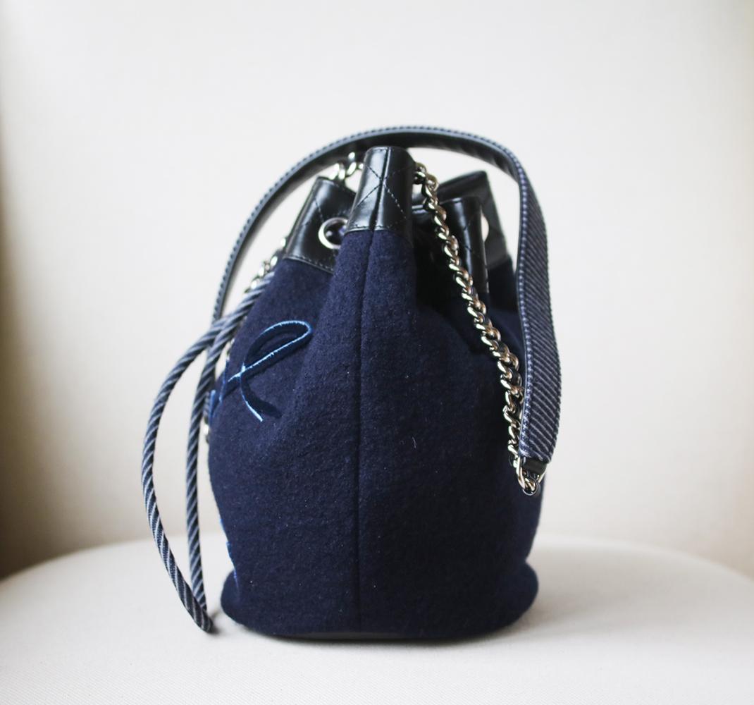 Chanel Drawstring Bag from Métiers D’art Paris-Hamburg 2018 Collection. Crafted from navy embroidered wool. Features chain link strap with shoulder pad. Embroidered Chanel writing on front. Silver-tone hardware. Drawstring closure. Black nylon