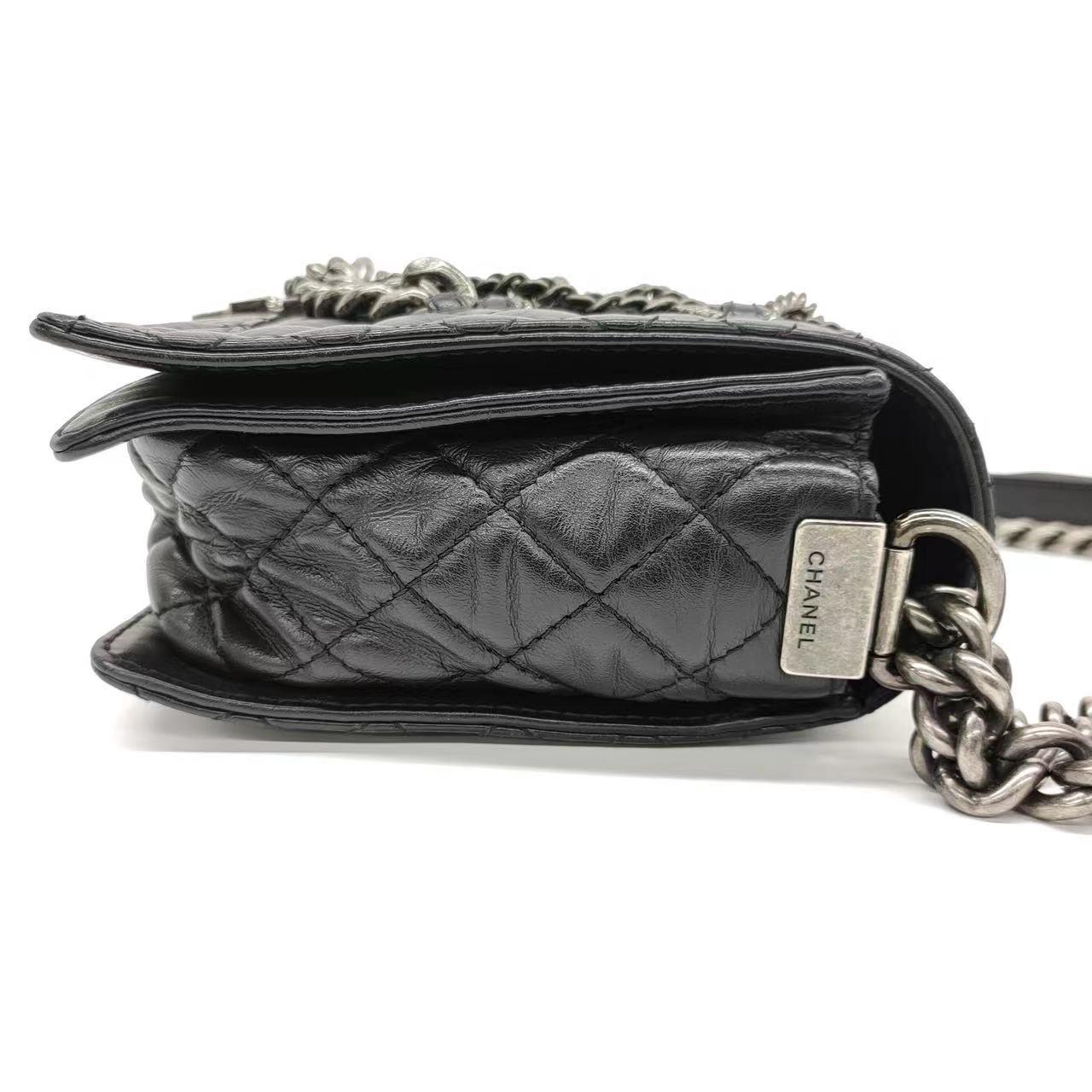 Diese Chanel Enchained Boy Bag ist aus schwarzem Lammleder gefertigt und mit silbernen Rotgussketten verziert. Sie ist sowohl stilvoll als auch funktional. Das ikonische Knabenschloss und die berühmte Chanel-Diamantensteppung zieren das Äußere,