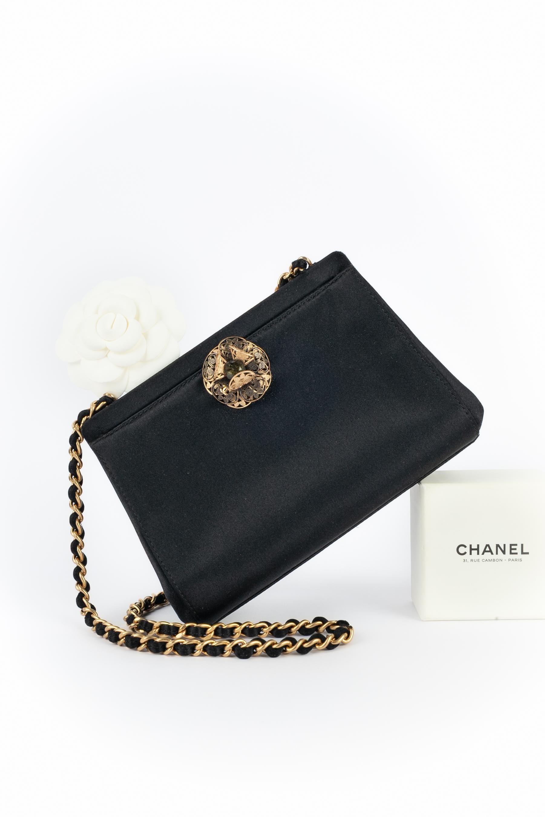 CHANEL - (Made in Italy) Bolso de noche de seda negra con cierre de camelia calada de metal dorado rematada con un strass, y con asa de cadena de metal dorado. Pieza con un número de serie y una tarjeta de autenticidad. Colección 2000-2002 bajo la