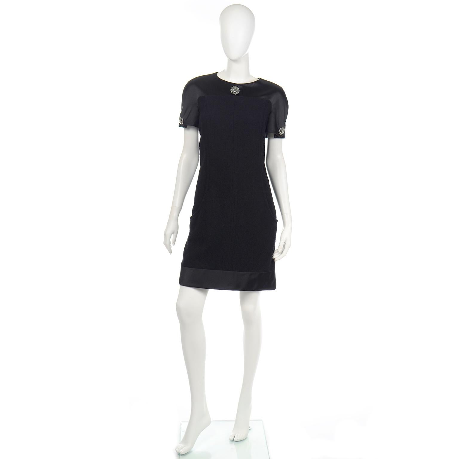 This is a lovely Chanel Fall 2015 dress in black bouclé wool and silk. The body of the dress is in bouclé wool and black silk satin is found at the hem and on the upper bodice and sleeves. There are beautiful gripoix buttons including one in the