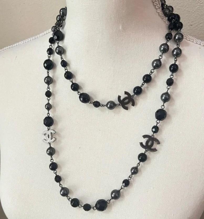 Collana di perle finte nere Chanel usata, realizzata in tonalità argento.

La collana presenta perle nere finte da 10 mm con perle sfaccettate rotonde e nere da 8 a 12 mm. Quattro loghi CC separano le perline.

La collana può essere indossata come