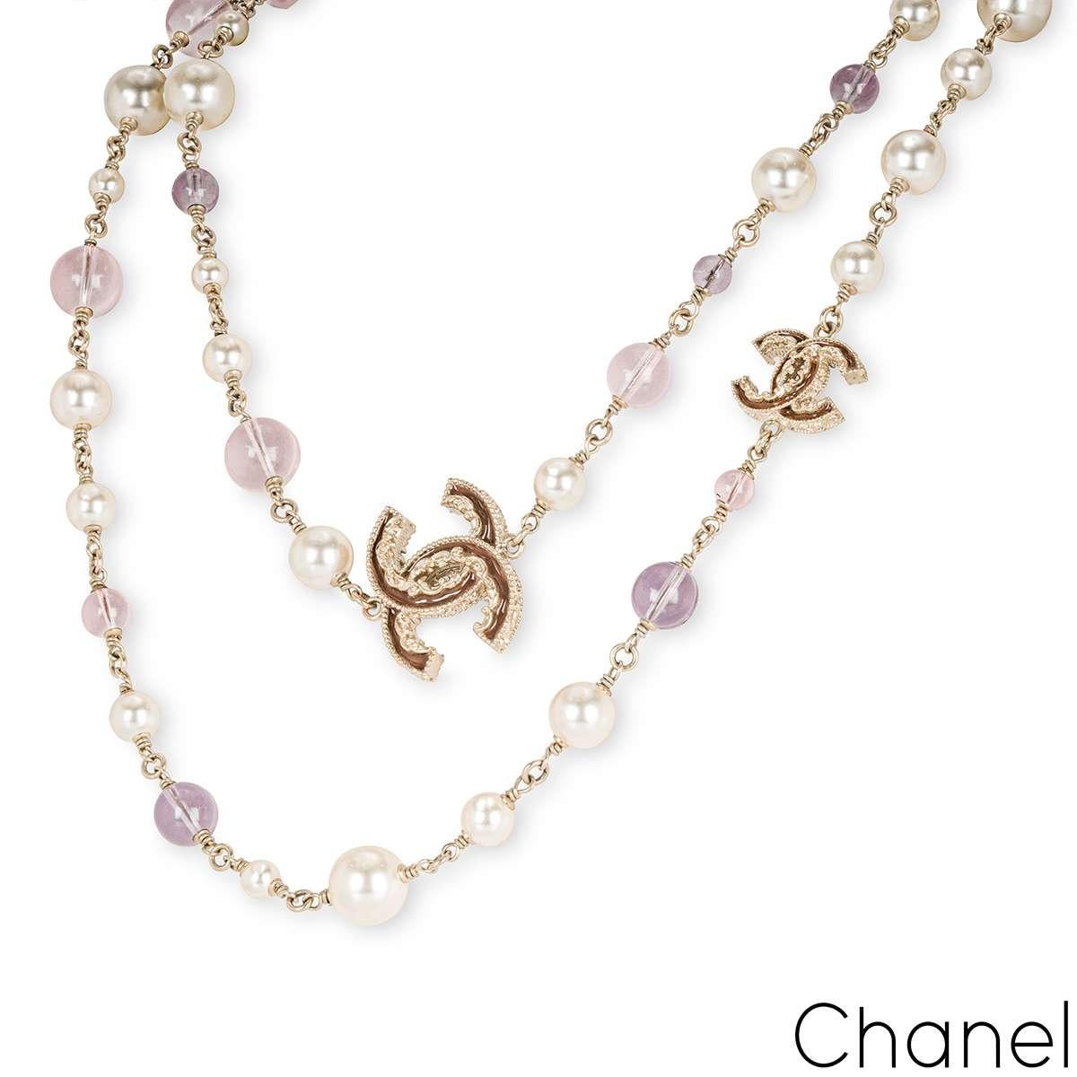 A chic champagne-tone faux pearl and glass bead station necklace by Chanel. The necklace is set throughout with 35 faux pearls, 10 pink glass beads and 7 purple glass beads. Adding to the allure of the necklace are two filigree enamel 'CC' stations