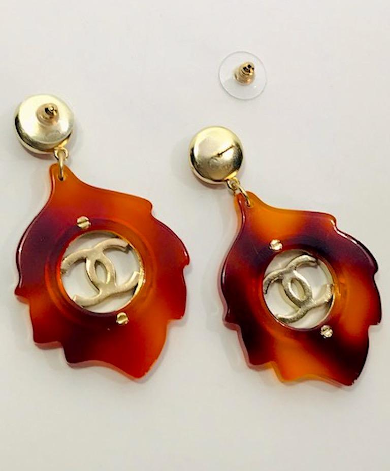 A lovely pair of faux tortoise pendant earrings with gold disk centers from the Chanel 2016 collection. Button top has an amber lucite cabochon that matches the light and dark amber leaf shape lucite pendant. Cast gold tone cutout interlocking CC