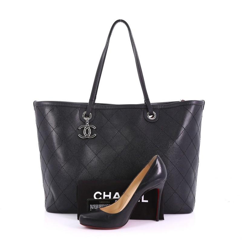 This Chanel Fever Tote Quilted Caviar Large, crafted in black quilted caviar leather, features dual-slim leather handles, leather trim, a Chanel CC charm, protective base studs, and silver-tone hardware. It opens to a burgundy fabric interior with