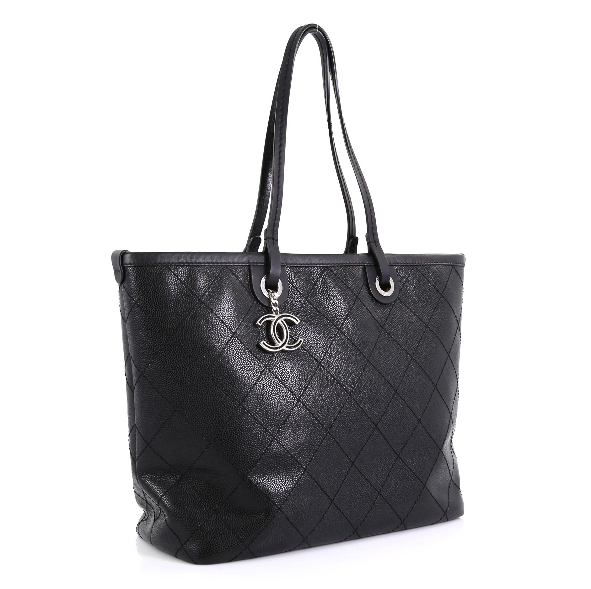 This Chanel Fever Tote Quilted Caviar Medium, crafted in black quilted caviar leather, features dual slim leather handles, CC charm, protective base studs, and silver-tone hardware. Its zip closure opens to a red fabric interior with zip and slip