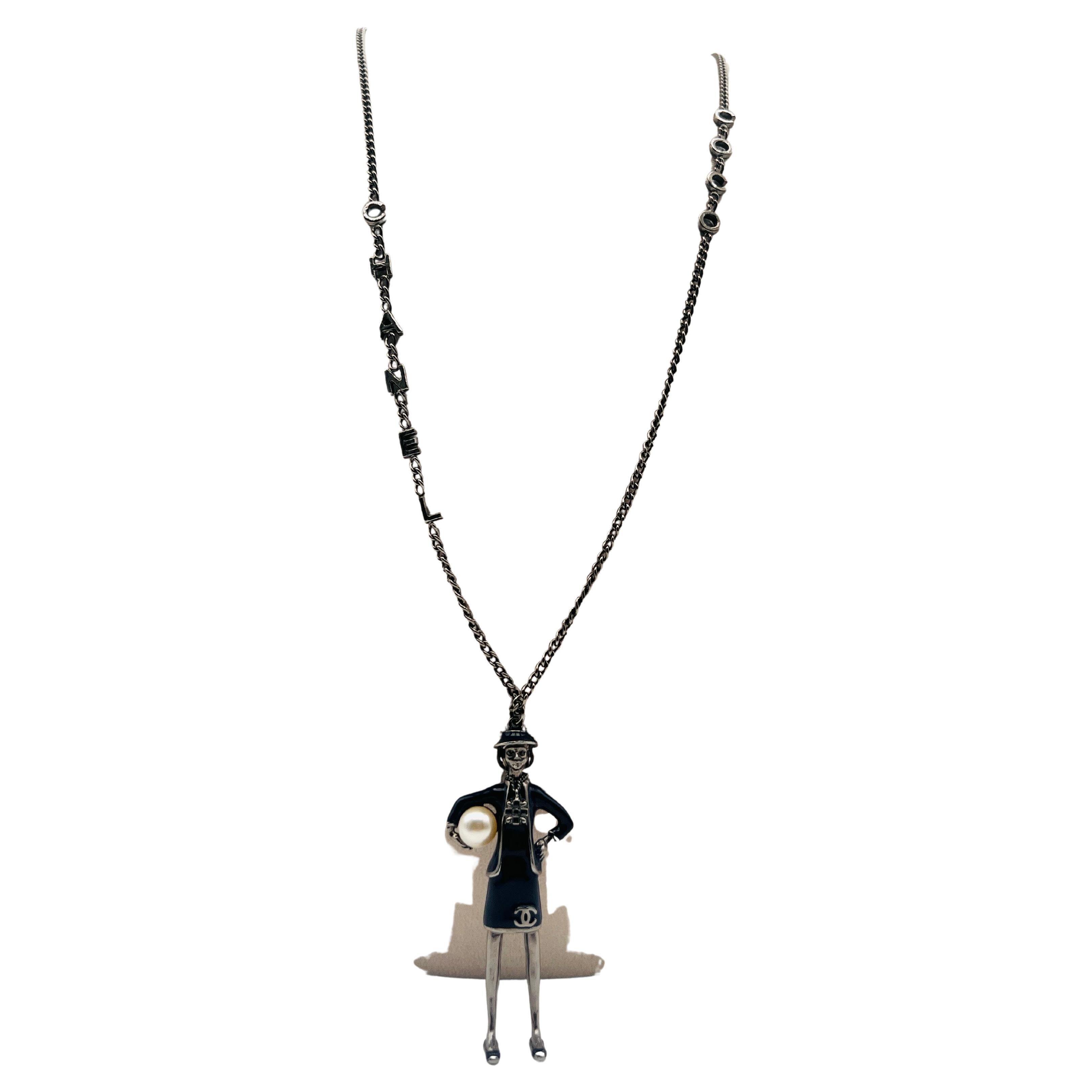 Sautoir Chanel automne 2012 COCO d'un côté CHANEL de l'autre, Gabriel Chanel portant un tailleur Chanel et un chapeau iconique tenant une perle sous le bras en pendentif figurine en émail bleu.
Tampon au dos Chanel 2012 Made in France.