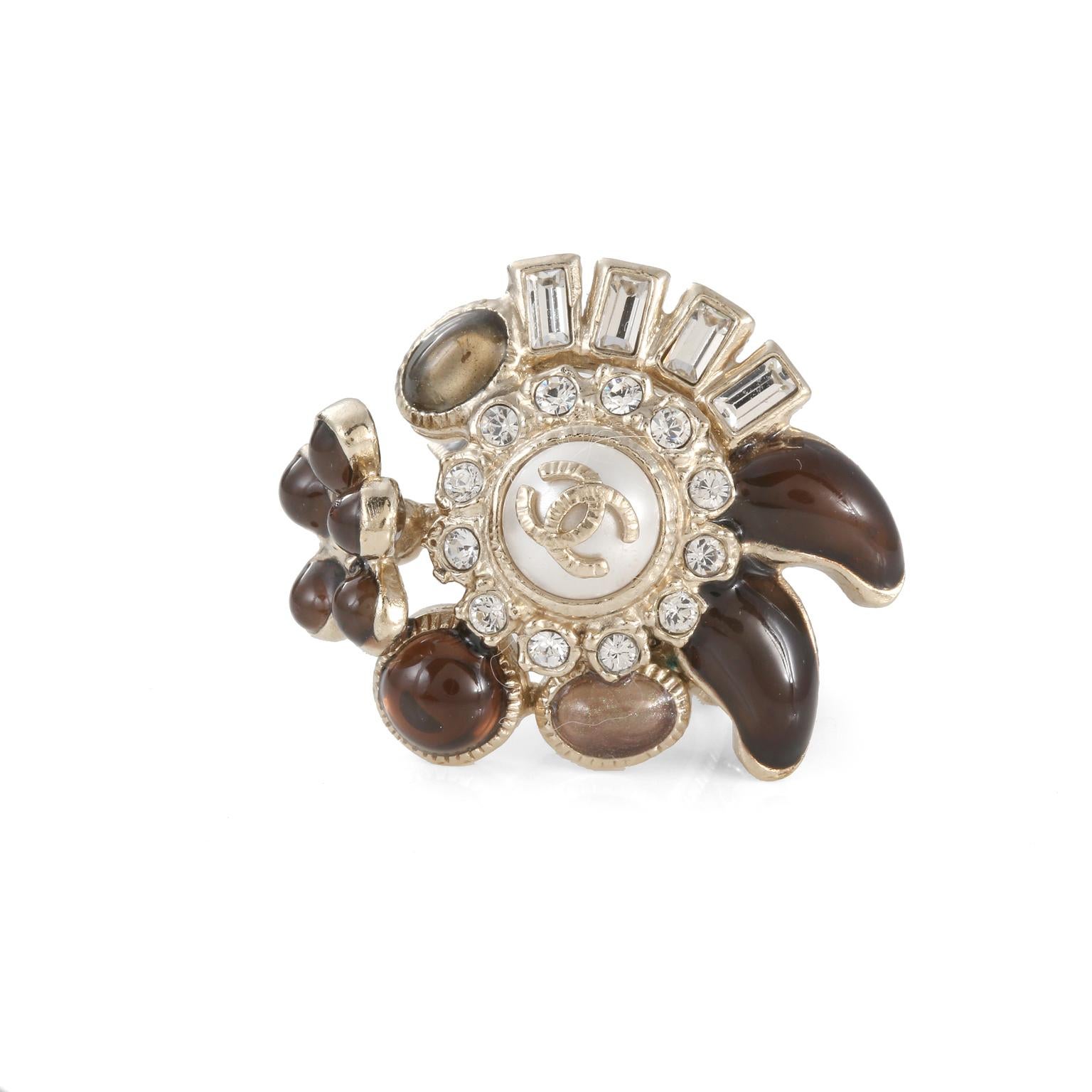 This authentic Chanel Flower Ring is in excellent condition.  Faux pearl center surrounded by crystals and glass stones in shades of neutral brown. Light gold tone finish with enamel.  Size 6. Pouch or box included.
