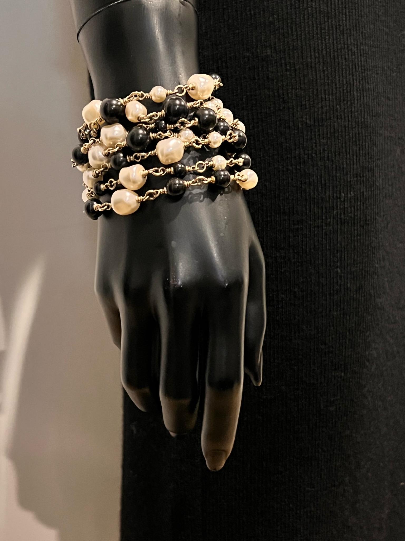 This is an authentic CHANEL Pearl and Black Beaded multi strand with gold chain. This elegant and elaborate cuff is accented with a double classic CC logo clasps. Adjustable size. 
This is a beautiful bracelet  in the timeless style of