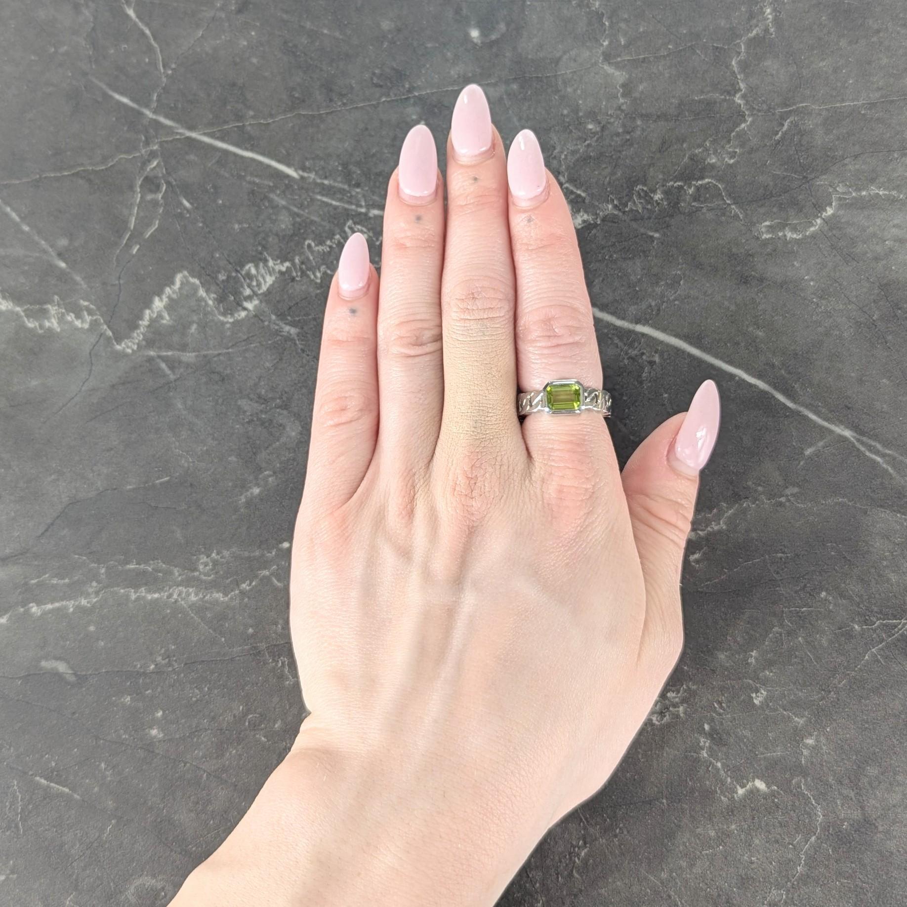 Centering an emerald cut peridot measuring 6.0 x 8.0 mm
Transparent medium green in color - bezel set
Flanked by curb link motif shank
Pierced and grooved with detail
Stamped with French hallmarks for 18 karat gold
Numbered and fully signed for