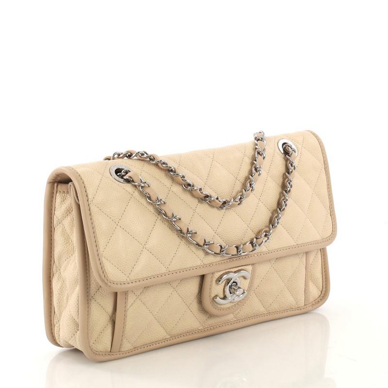 This Chanel French Riviera Flap Bag Quilted Caviar Medium, crafted from beige quilted caviar leather, features dual woven-in leather chain straps, leather trim, front flat pocket underneath flap, and silver-tone hardware. Its CC turn-lock closure