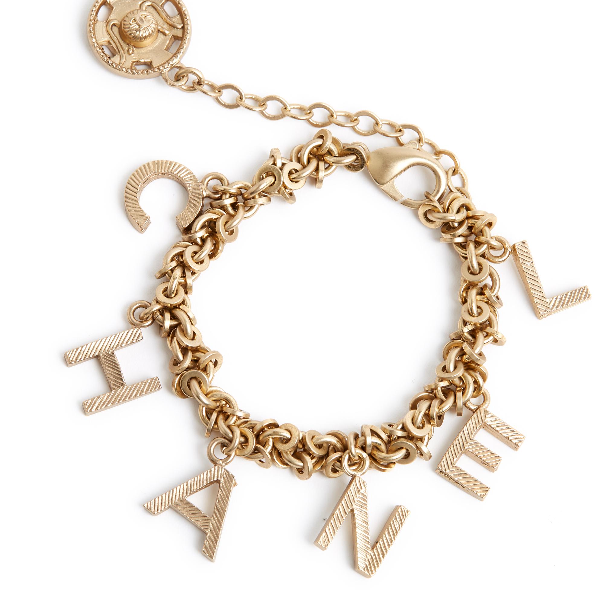 Armband Chanel Collection FW2003 aus mattgoldenem Metall, bestehend aus einer Kette mit runden Gliedern und Quasten mit Chanel-Schriftzug, Verschluss mit Karabinerhaken an einer Kette, die mit einem Nähverschluss mit CC-Logo endet. Länge des