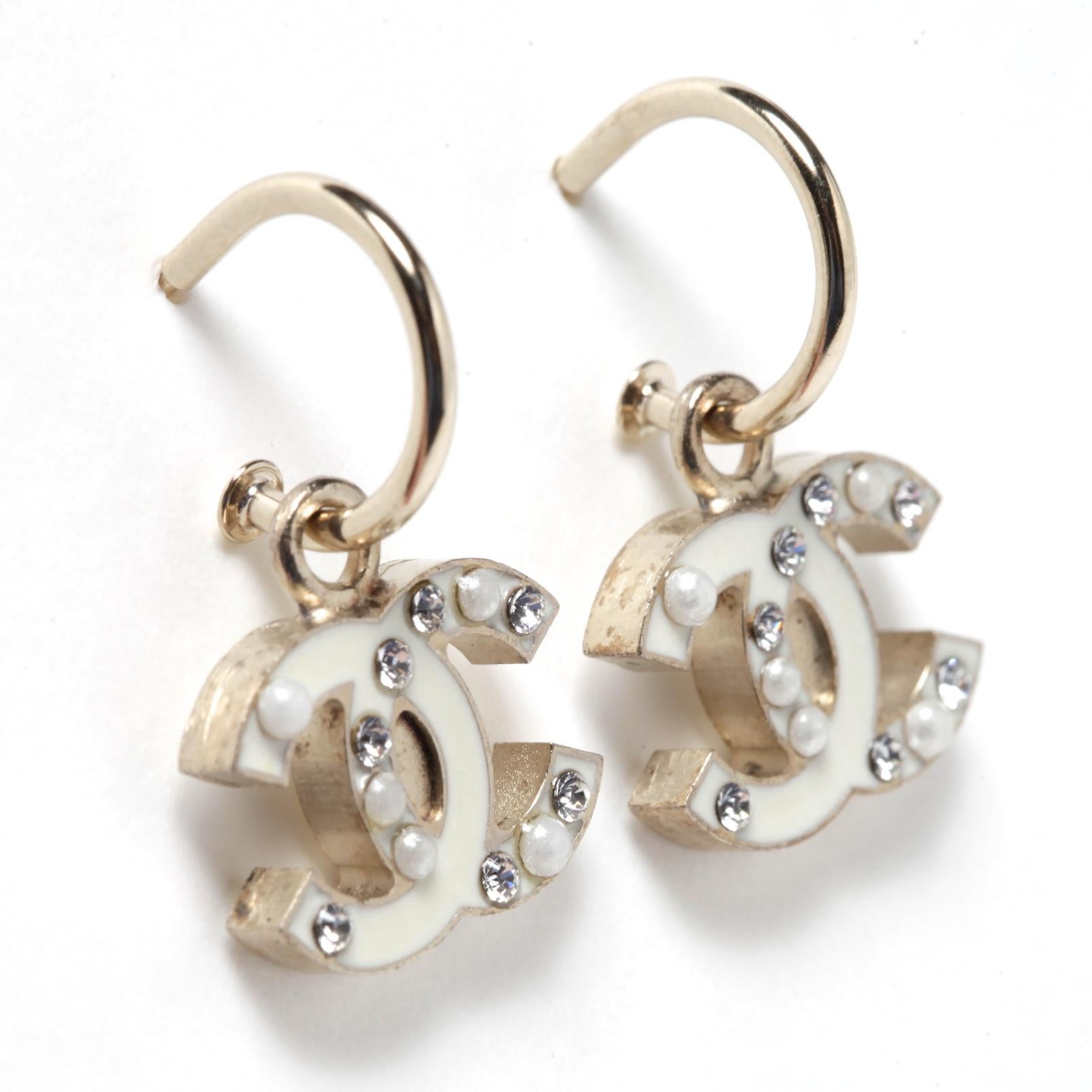 Chanel earrings composed of a small creole and a pendant with a Chanel logo motif in lightly gilded metal (between gold and silver) encrusted with white rhinestones and small fancy pearls, all enameled in ecru color. Total height of the earring 2.65