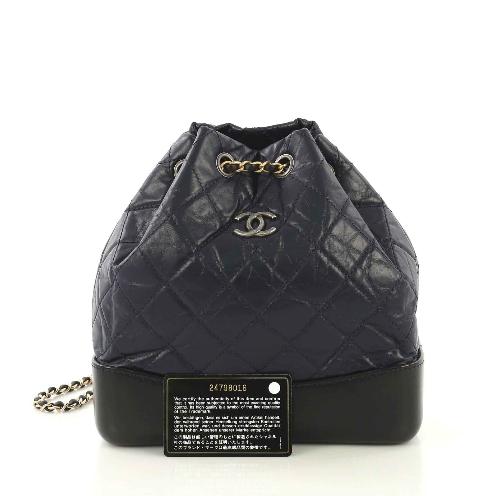 This Chanel Gabrielle Backpack Quilted Calfskin Small, crafted from black and blue quilted calfskin leather, features gradient woven-in leather chain straps threaded through eyelets, CC logo at front, and aged gold and aged silver tone hardware. It