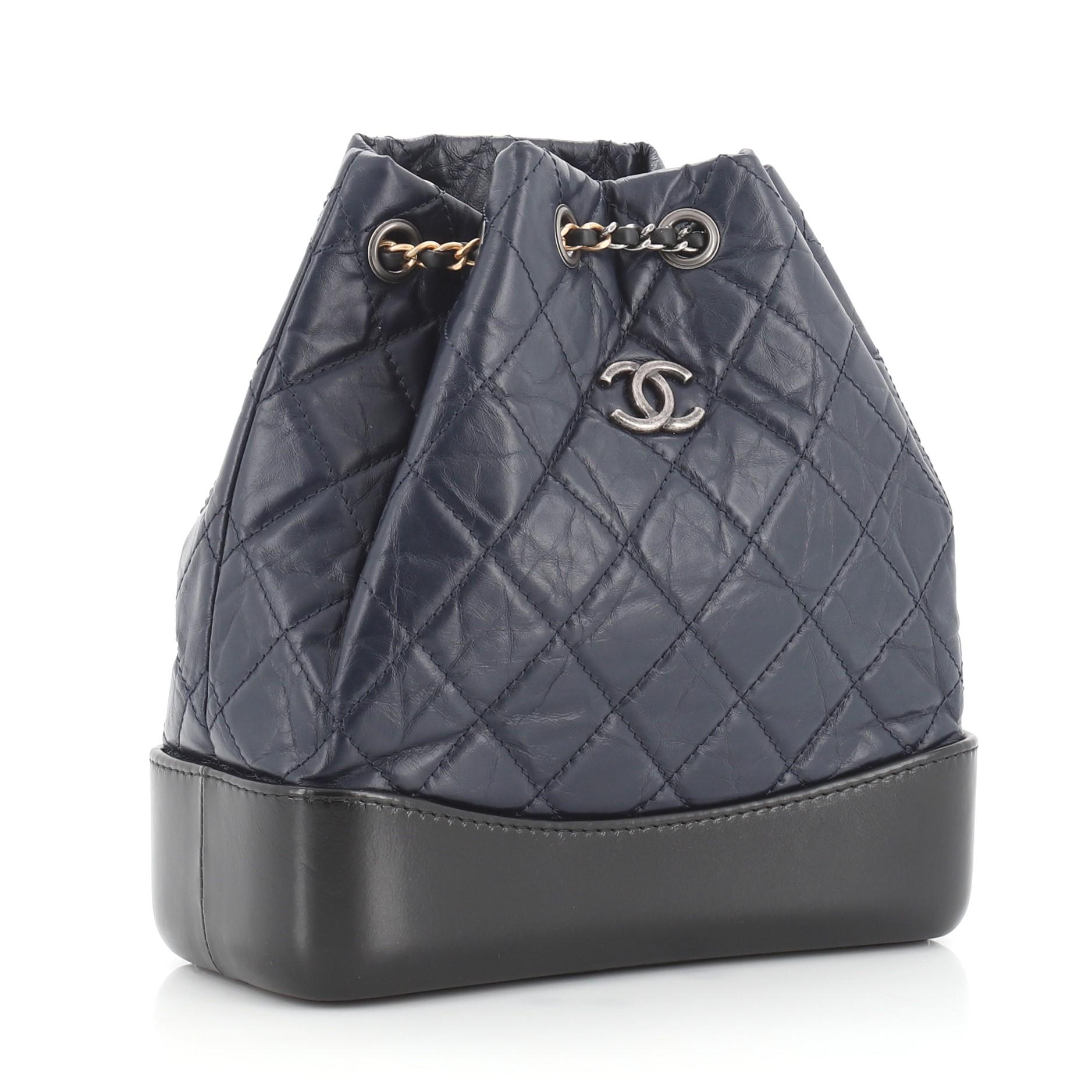 This Chanel Gabrielle Backpack Quilted Calfskin Small, crafted from black and blue quilted calfskin leather, features gradient woven-in leather chain straps threaded through eyelets, CC logo at front, and aged gold and aged silver tone hardware. It