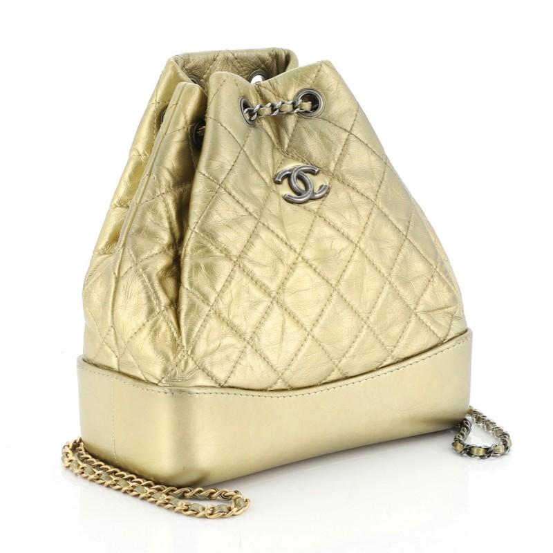 This Chanel Gabrielle Backpack Quilted Calfskin Small, crafted gold leather, features gradient woven-in leather chain straps threaded through eyelets, CC logo at front, and aged gold, silver and gunmetal-tone hardware. It opens to a red fabric
