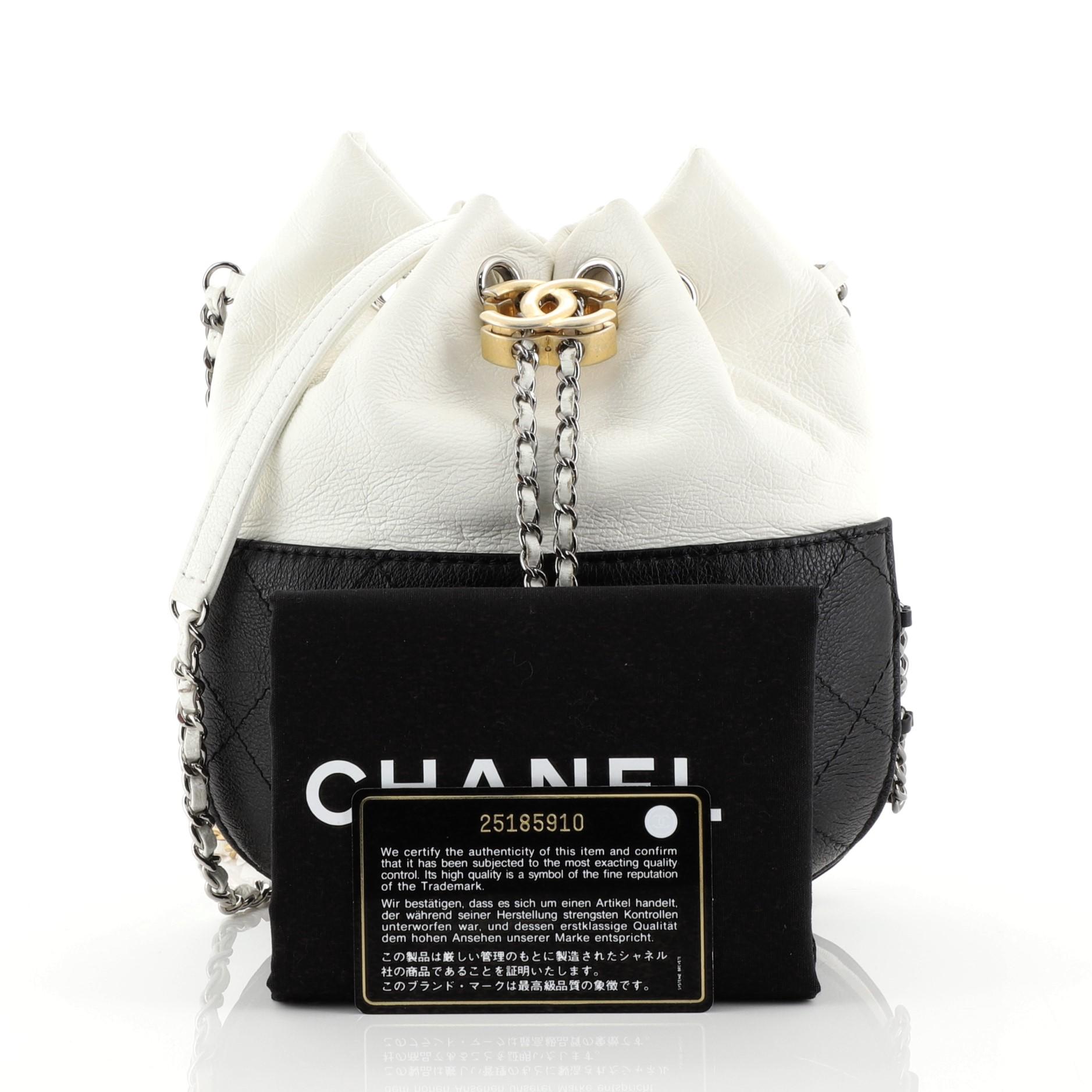 This Chanel Gabrielle Drawstring Bag Quilted Calfskin Small, crafted in white and black quilted calfskin leather, features woven-in leather chain strap with leather pad, drawstring with CC logo accent, and silver, gunmetal and gold-tone hardware.