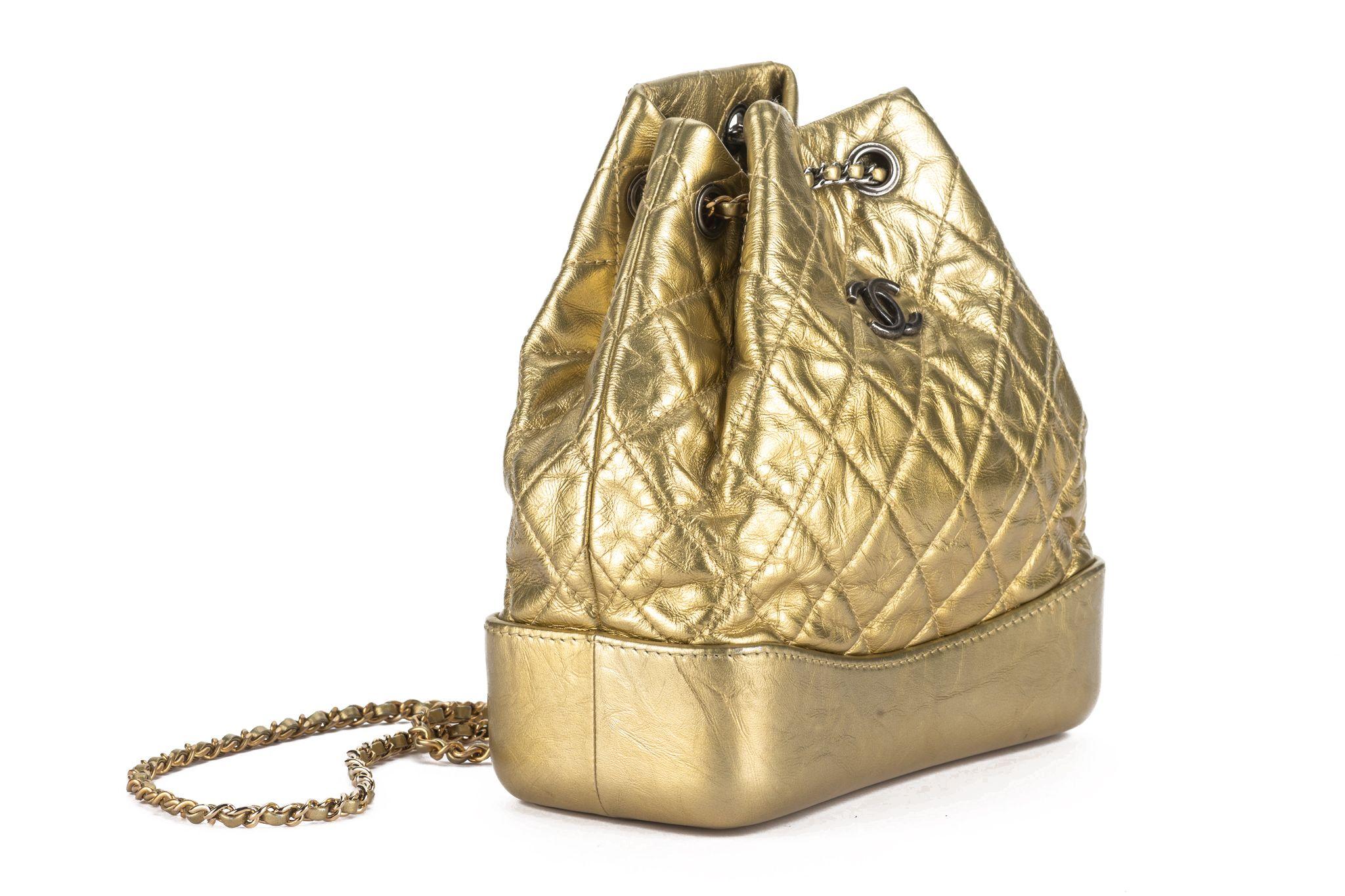 Chanel aged calfskin quilted small Gabrielle backpack in gold. This chic backpack is crafted of diamond quilted aged calfskin leather. The shoulder bag features a smooth leather base, a CC logo, polished gold and silver chain threaded leather
