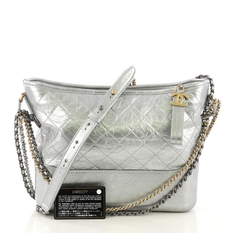 This Chanel Gabrielle Hobo Quilted Aged Calfskin Medium, crafted from silver quilted aged calfskin leather, features woven-in leather chain strap with leather pad, leather zip pull with CC logo, and gold, aged silver and silver-tone hardware. Its