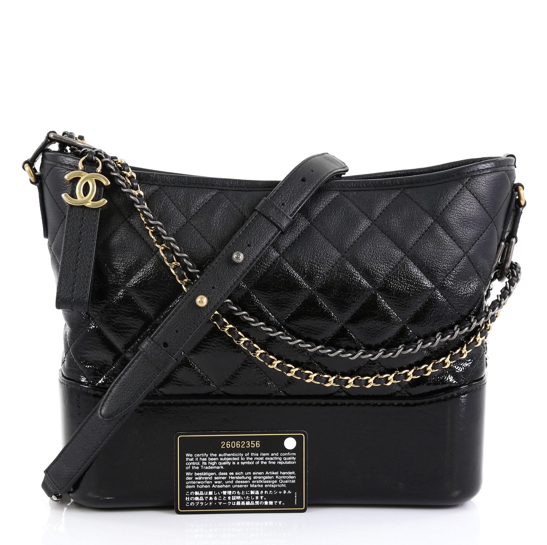 This Chanel Gabrielle Hobo Quilted Goatskin and Patent Medium, crafted from black quilted goatskin and patent leather, features woven-in leather chain strap with leather pad, leather zip pull with CC logo, and aged silver-tone hardware. Its zip