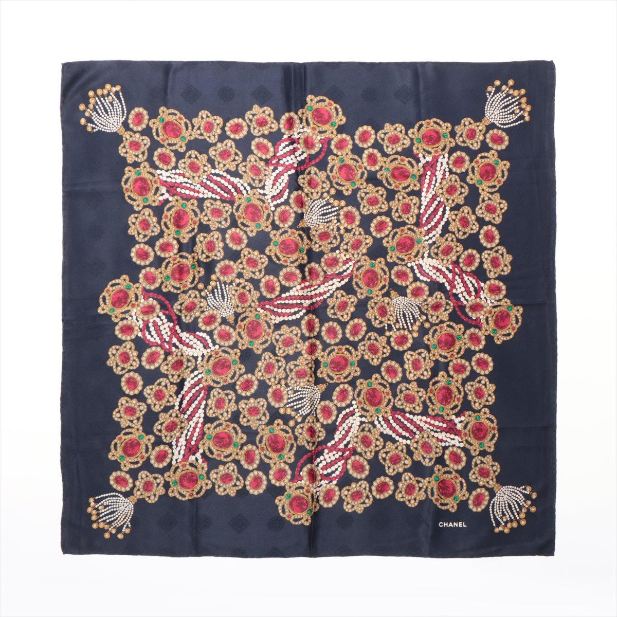 The Chanel Gems and Pearl Silk Scarf in navy blue is a stunning accessory that showcases the brand's timeless elegance. Made from luxurious silk, the scarf features a captivating design of red gems and pearls set against a deep navy blue background,