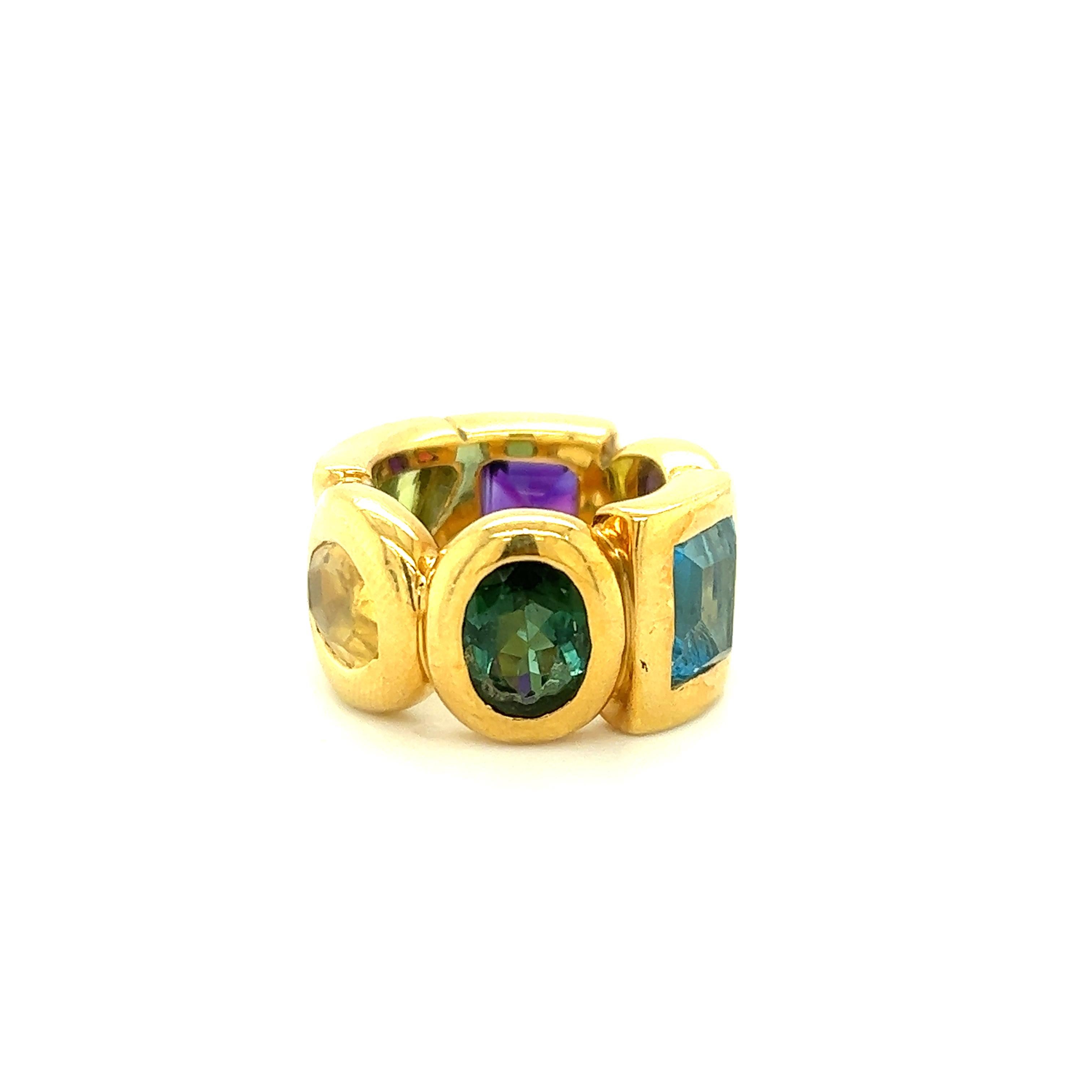 Fantastic ring crafted by famed designer Chanel in 18k yellow gold. The ring is a wide band design and decorated with semi precious gemstones throughout. The ring shows geometric shapes crafted throughout the 18k metal design in triangle, square,